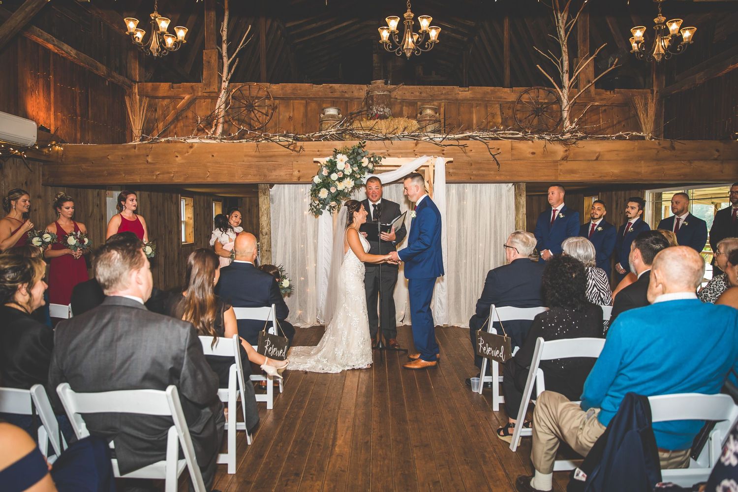 Rustic barn wedding venue decorated with chandeliers and white drapery for ceremony.