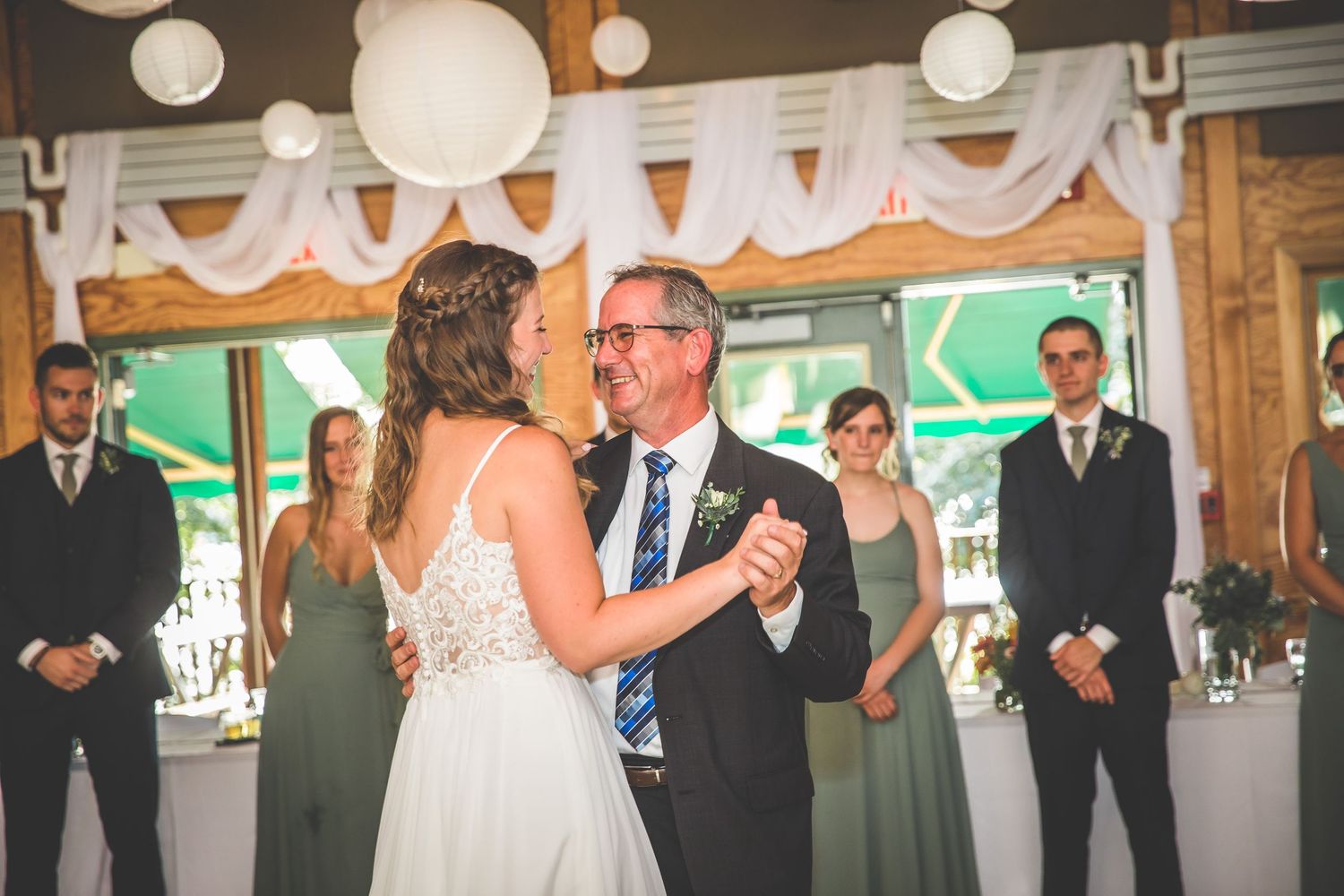 Wedding party dances beneath elegant white draping and paper lanterns in rustic venue.