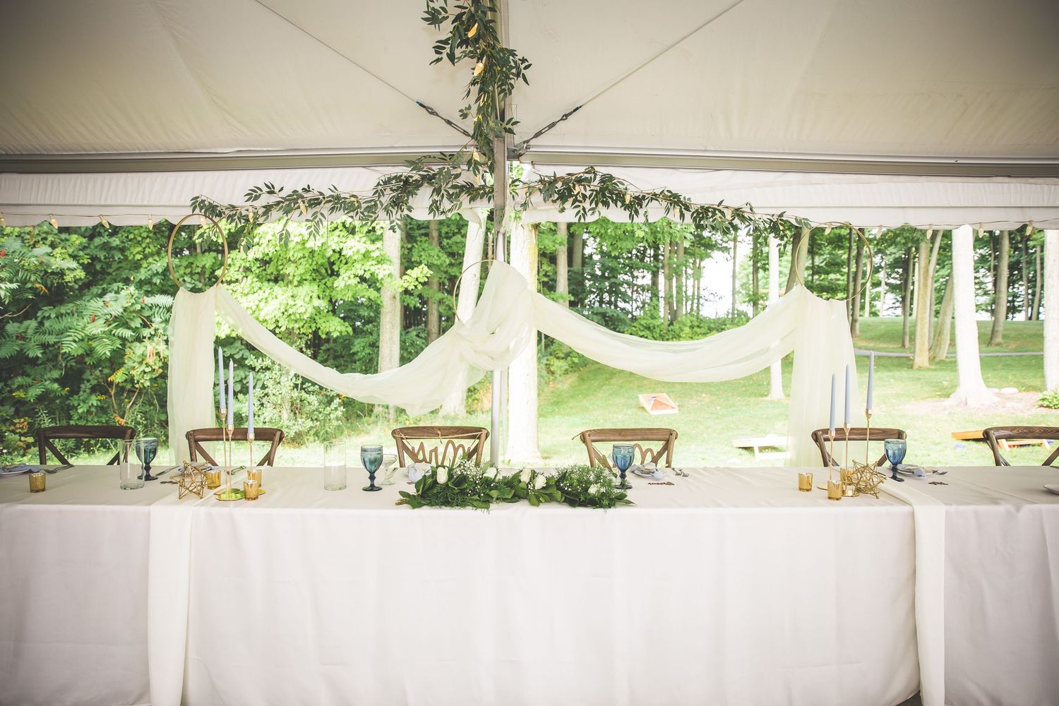 Wide view of an outdoor wedding reception tent with white draping and rustic wooden chairs.
