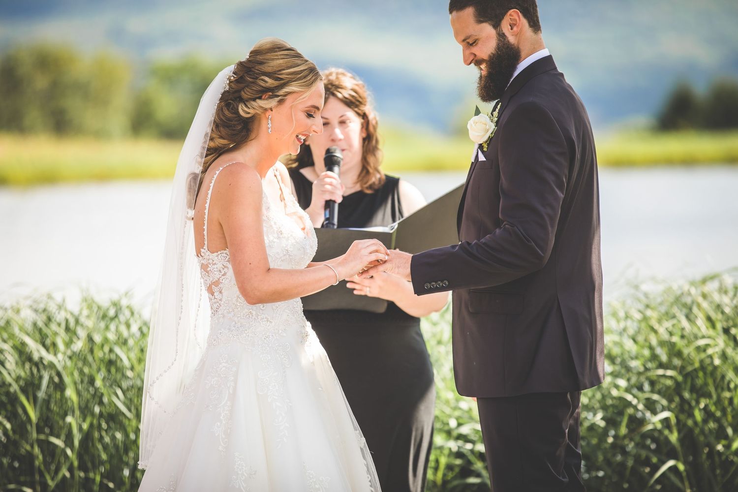 A wedding ceremony takes place outdoors with a scenic view of fields and mountains in the background.