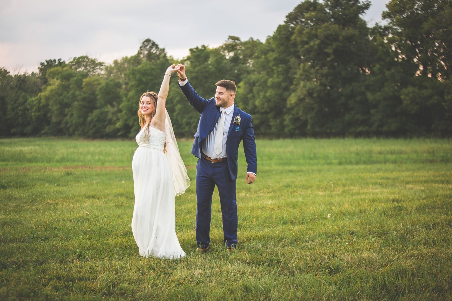 Couple walking hand in hand through a lush green field at sunset.