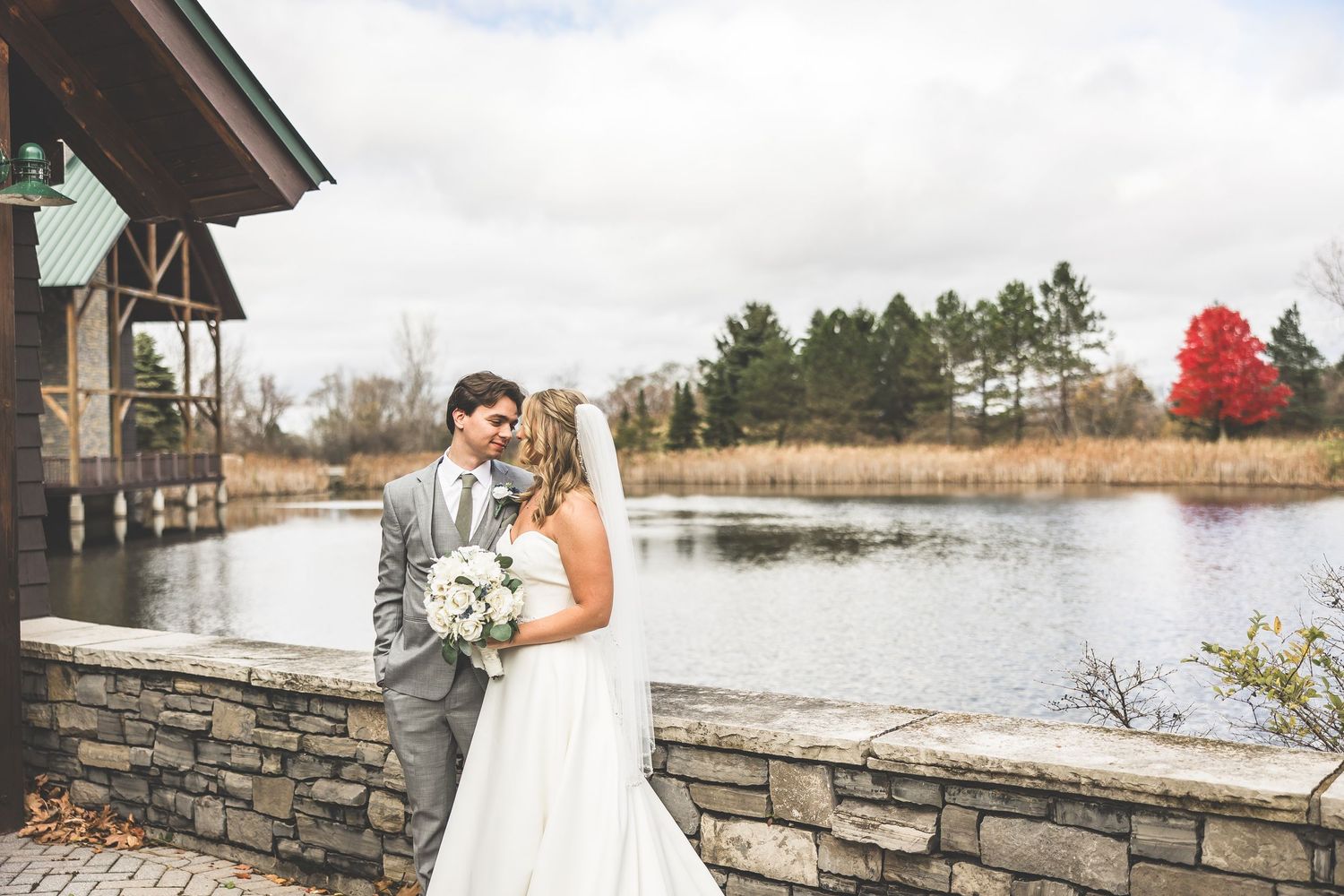 Wedding venue deck overlooking lake with stone wall and autumn trees.