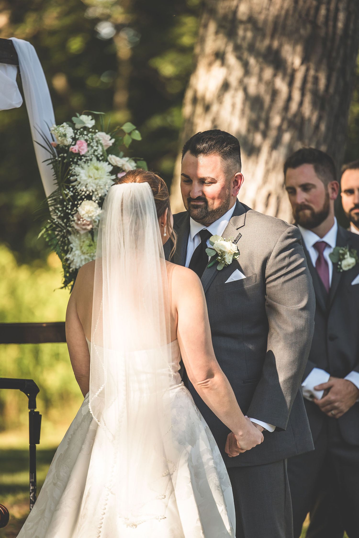 Wedding ceremony with groomsmen in dark suits standing under decorated arch.