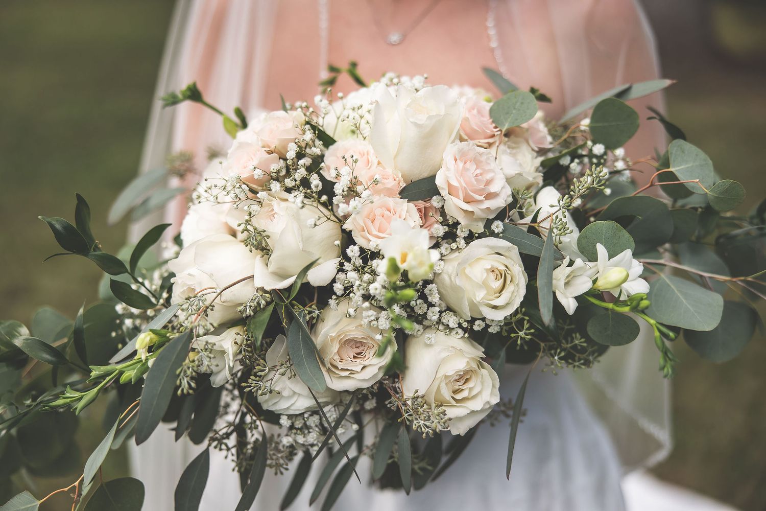 Close-up of romantic white and blush pink wedding bouquet with roses and eucalyptus leaves.