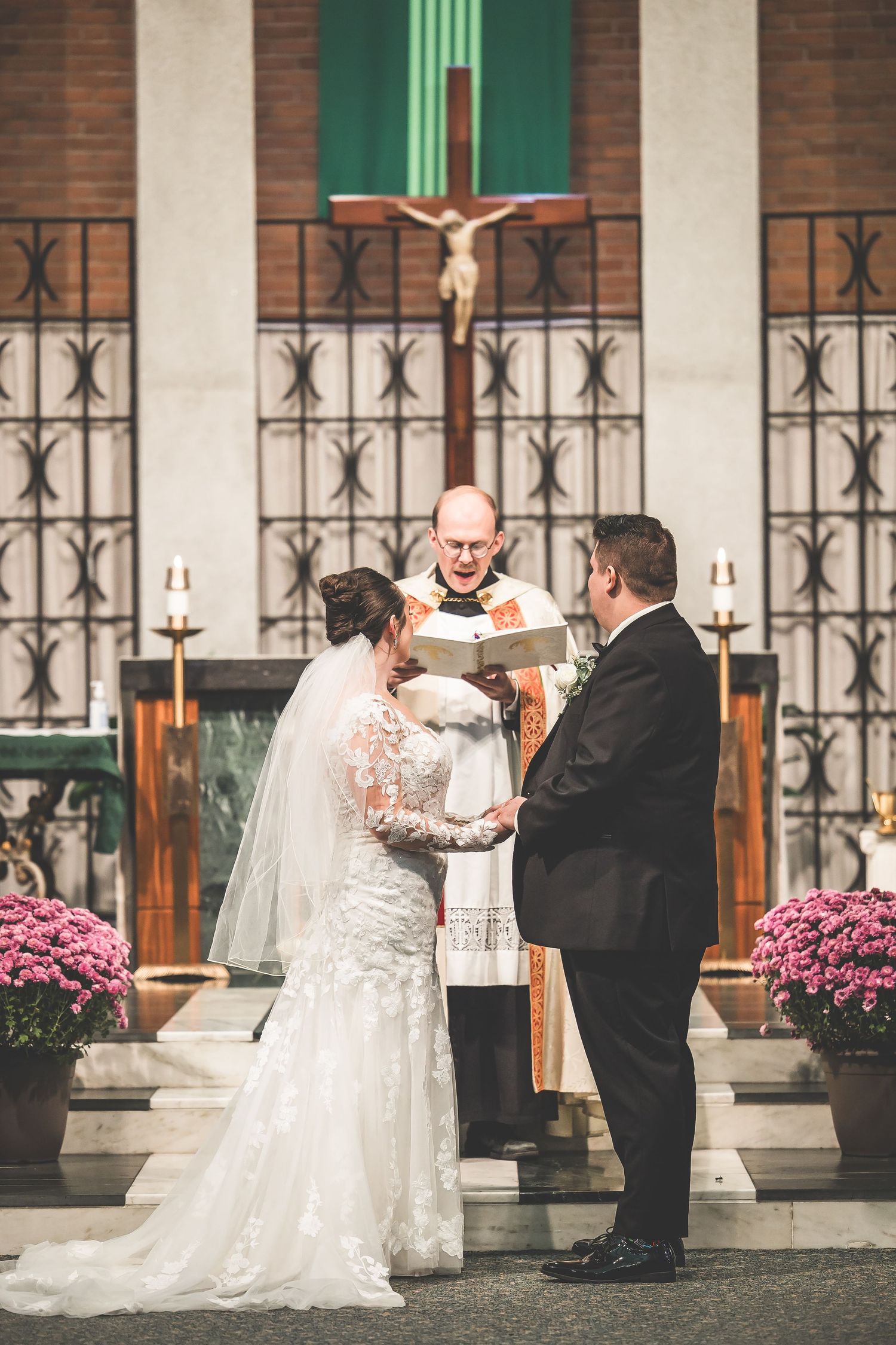 Wedding ceremony taking place at altar with pink floral arrangements and iron window details.