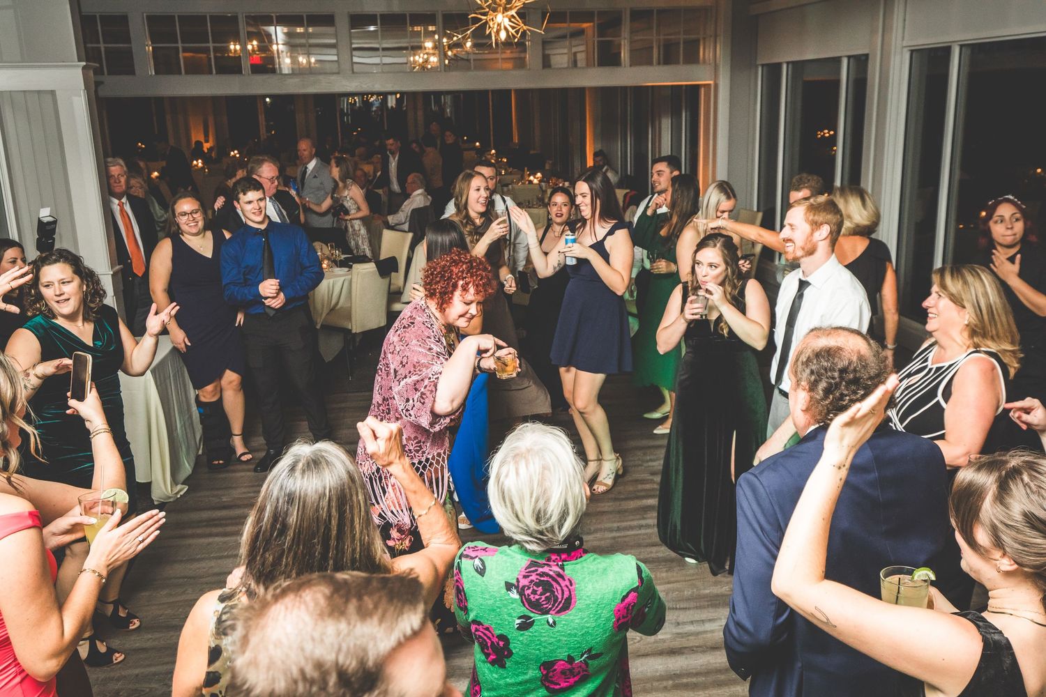 Wedding reception dance floor filled with guests celebrating under ambient lighting.