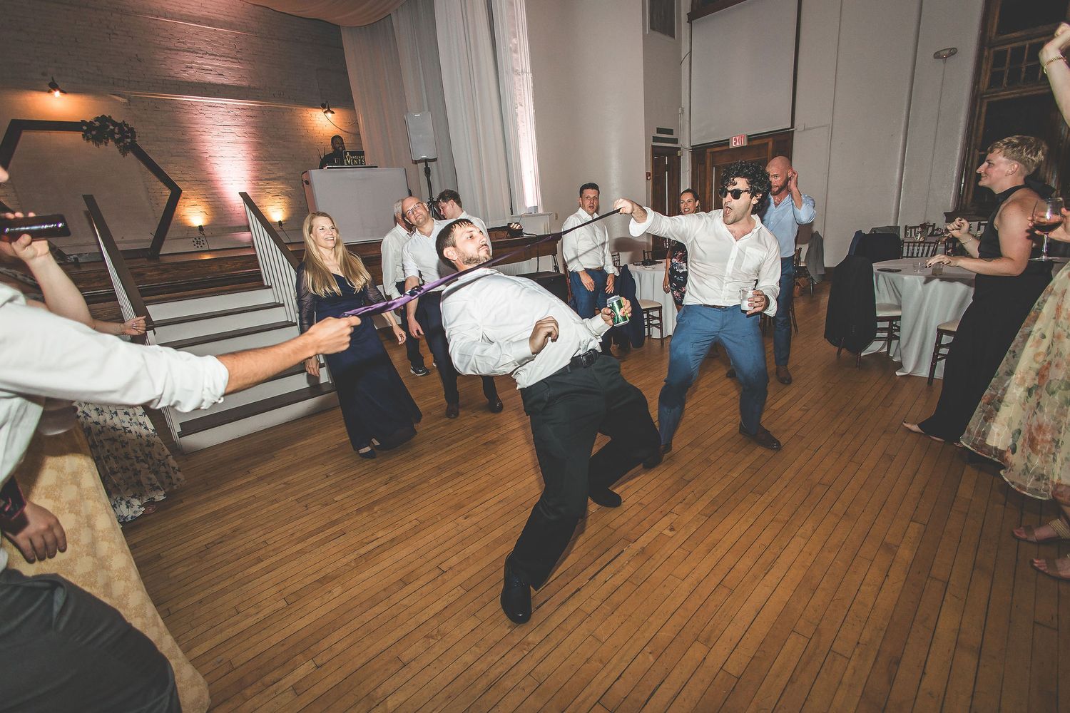 Wedding guests dancing energetically on a wooden dance floor during evening reception celebrations.