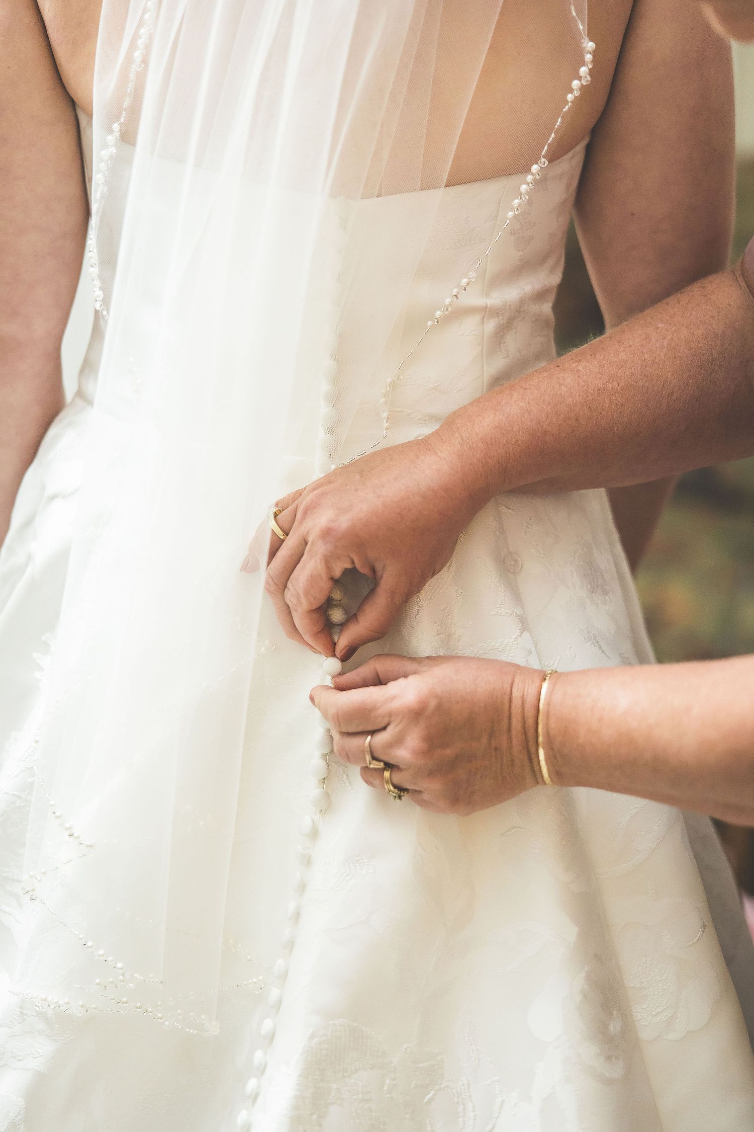 Close-up shots of hands adjusting a white wedding dress in natural lighting.