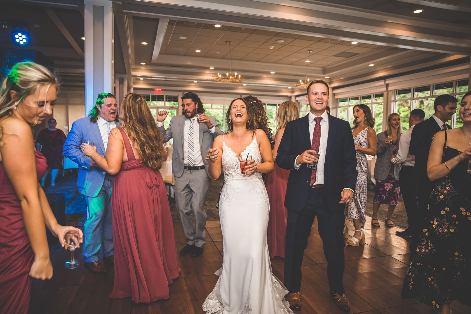 Large group dancing together at an elegant wedding reception with chandeliers and mood lighting.