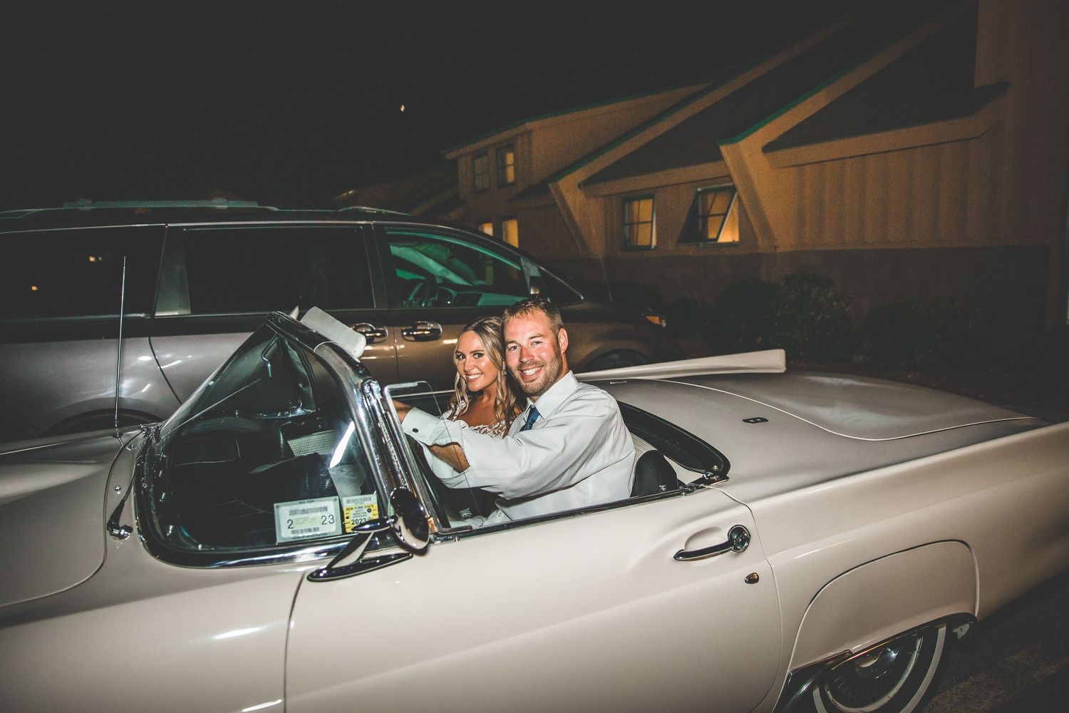 Newlyweds posing with vintage car at night during wedding exit.