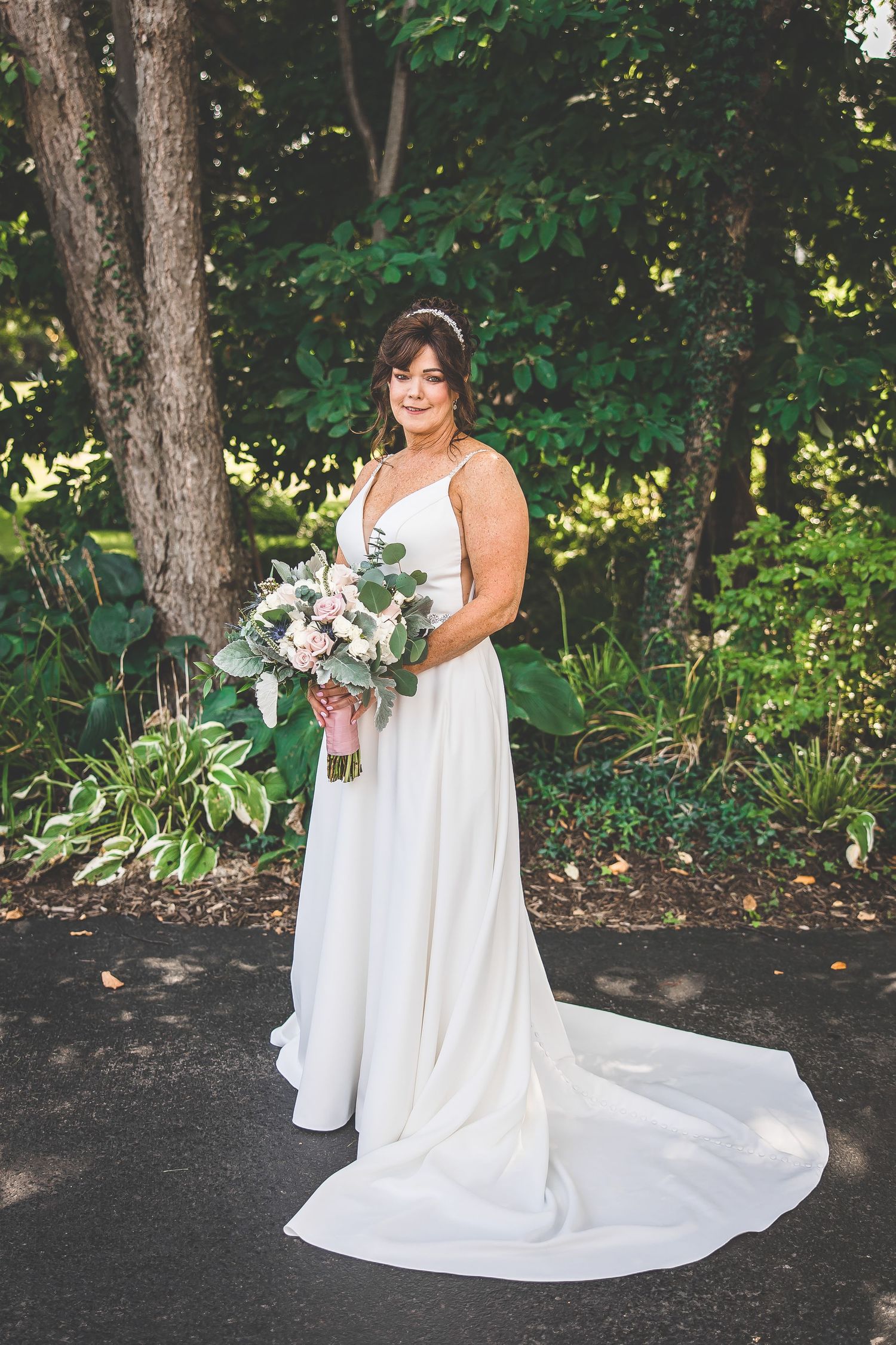 Bride in flowing white dress holds bouquet in garden setting.