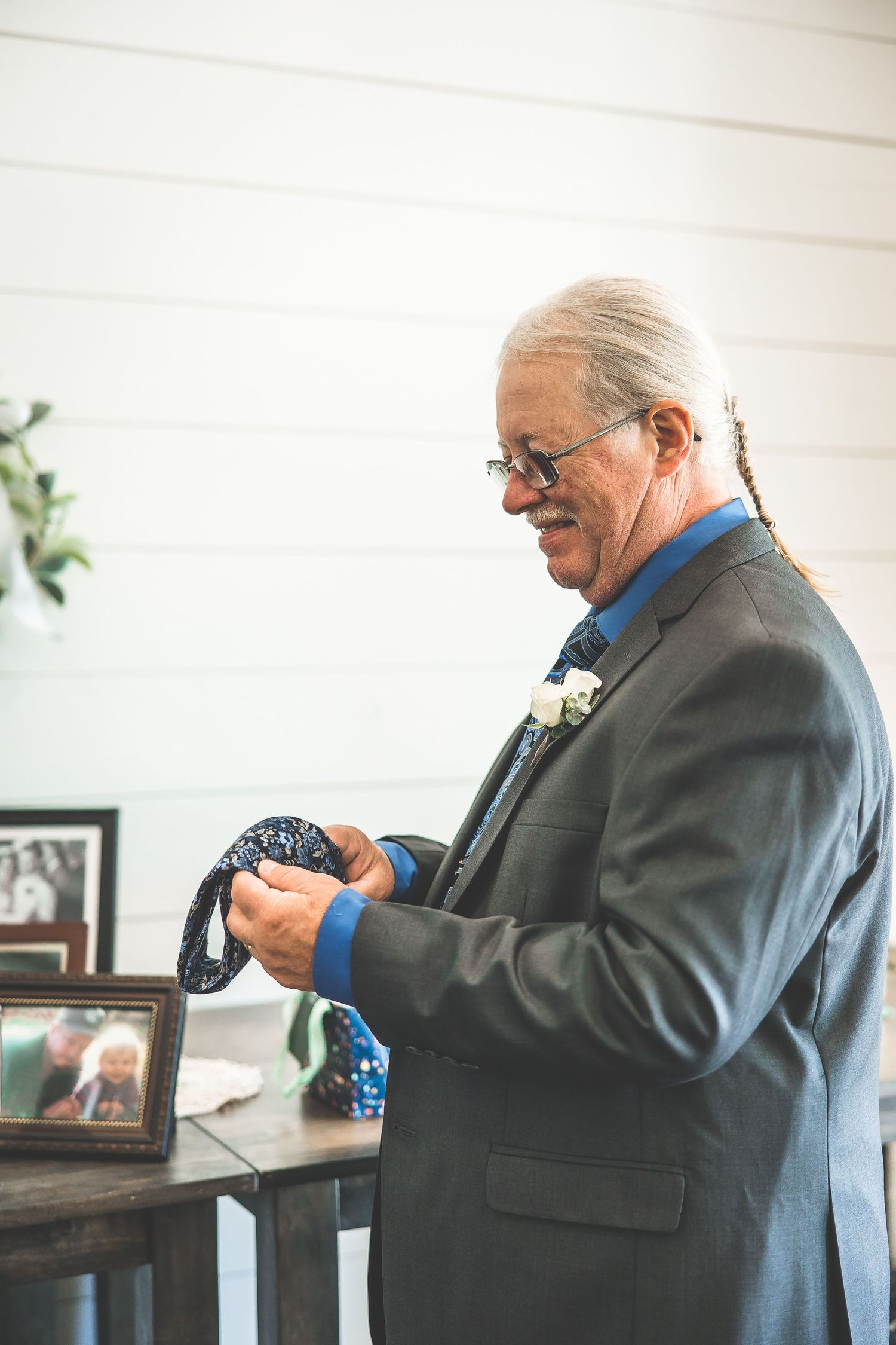 An elegant guest in a grey suit examines something in his hands by a window.