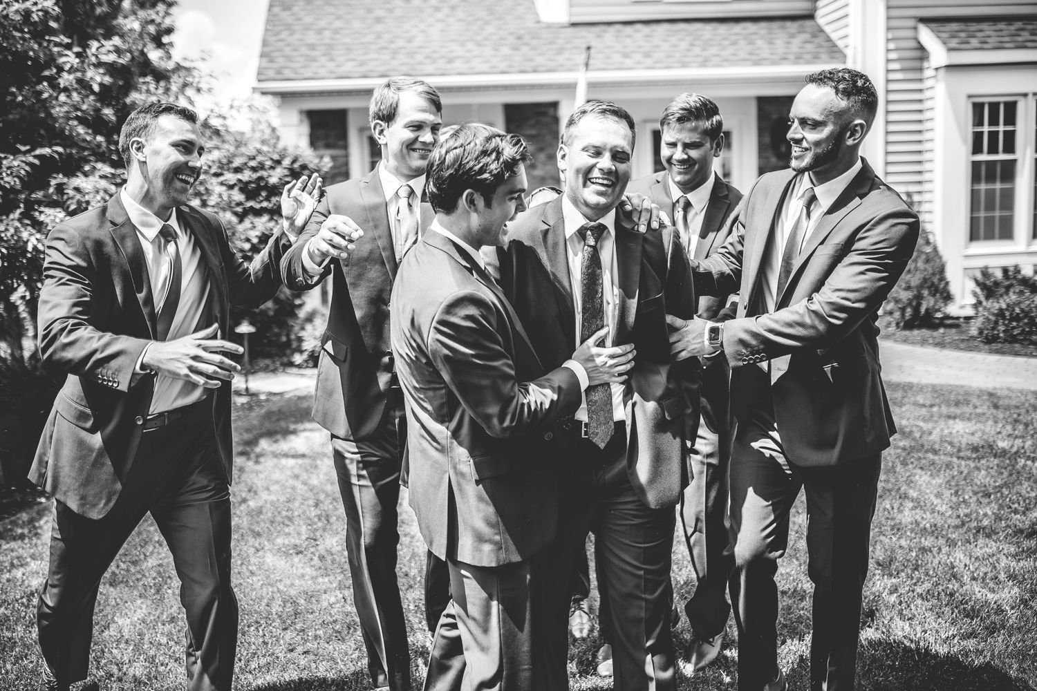 Wedding party members in dark suits posing casually on the lawn.