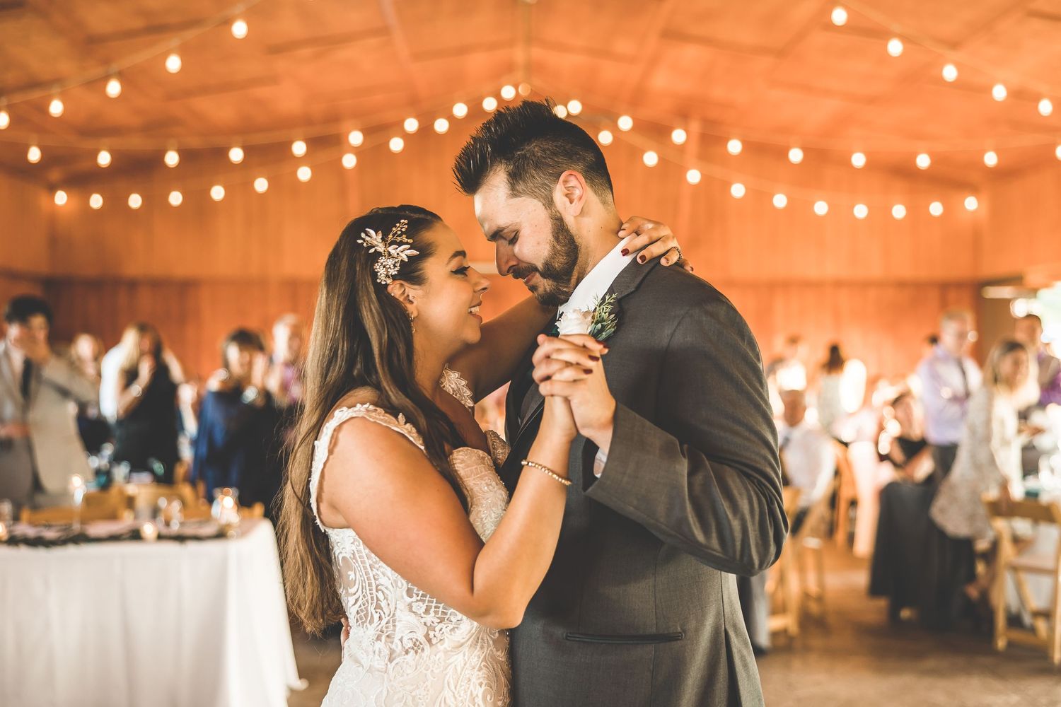 First dance at wedding reception with string lights creating warm ambiance in rustic venue.