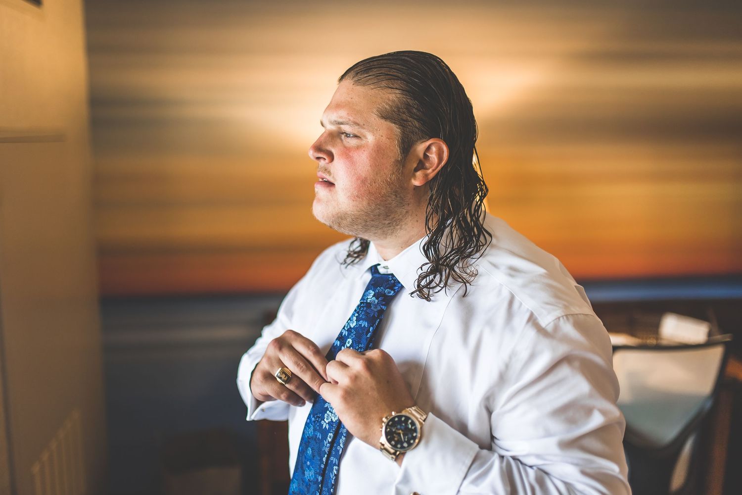 A person adjusts their blue tie while getting ready in formal attire.