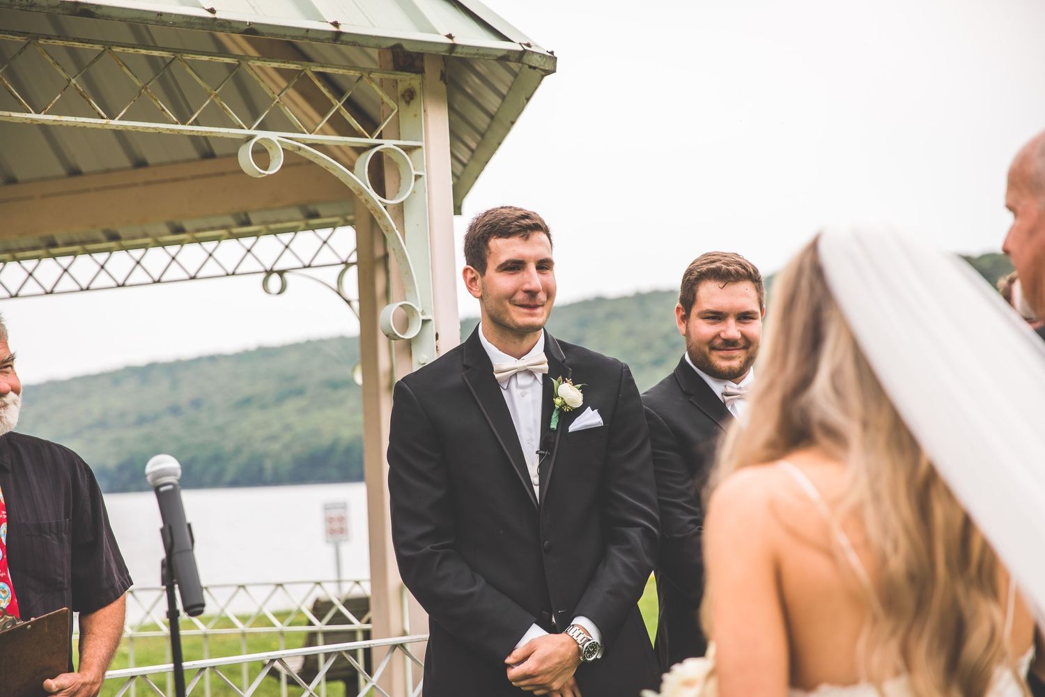Wedding ceremony under white gazebo overlooking scenic lake view.