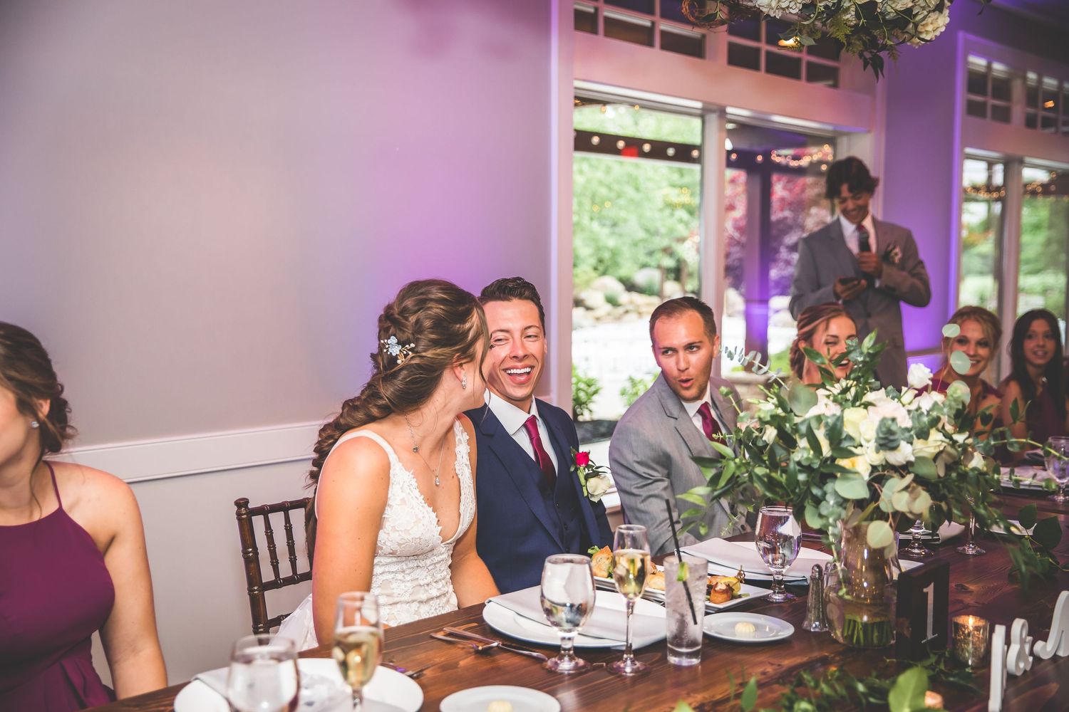 Wedding reception guests enjoying dinner and conversation at tables decorated with floral centerpieces.
