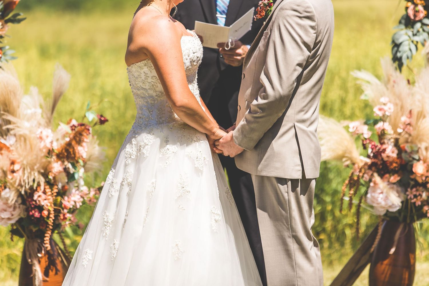 Intimate wedding ceremony moment under draped orange fabric in sunny field.