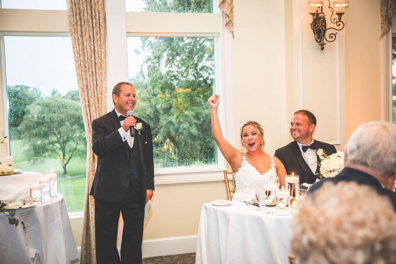 Wedding reception speech and celebration at an elegant venue with large windows.