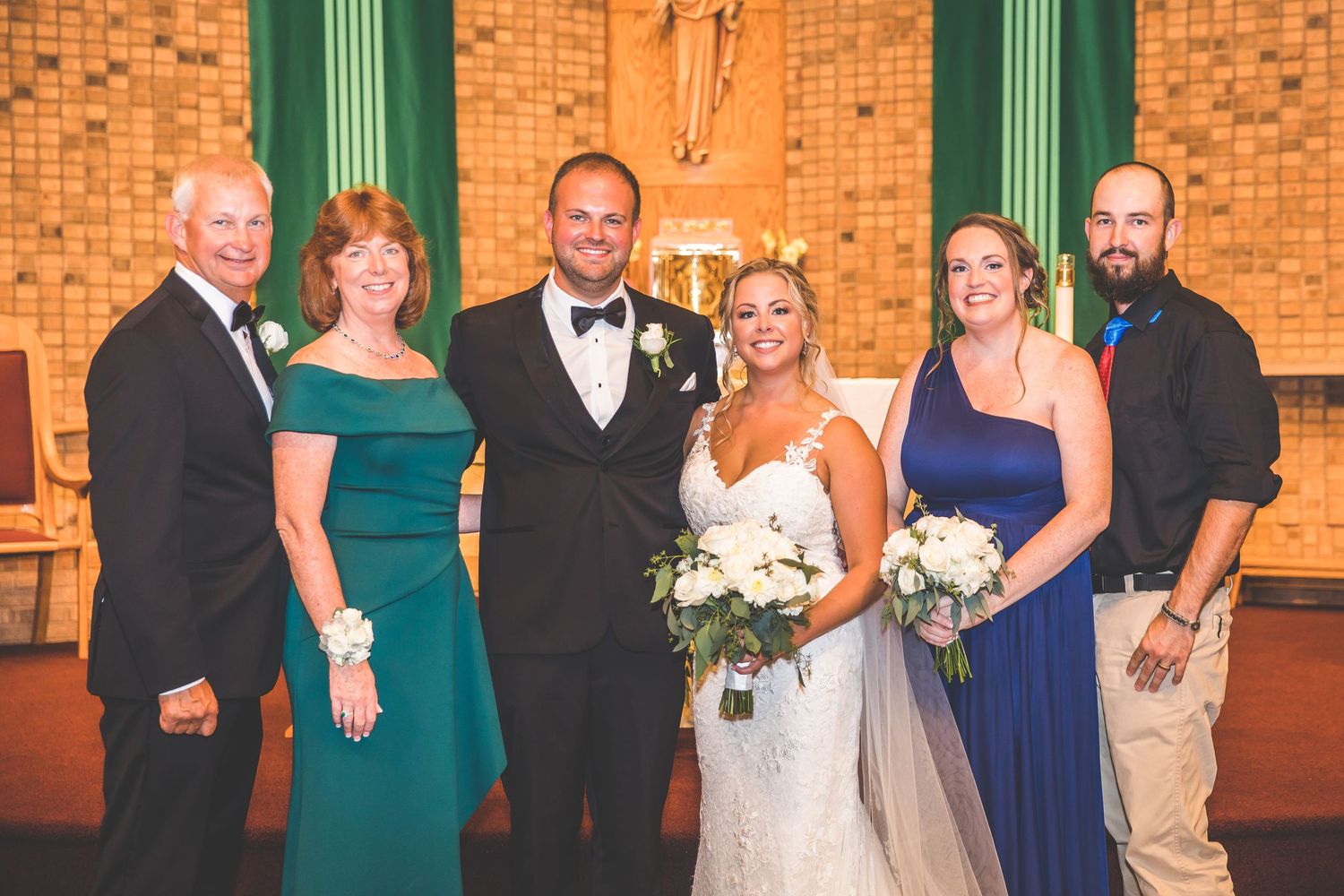 Wedding party members gather for formal portraits in front of decorative green church pillars.