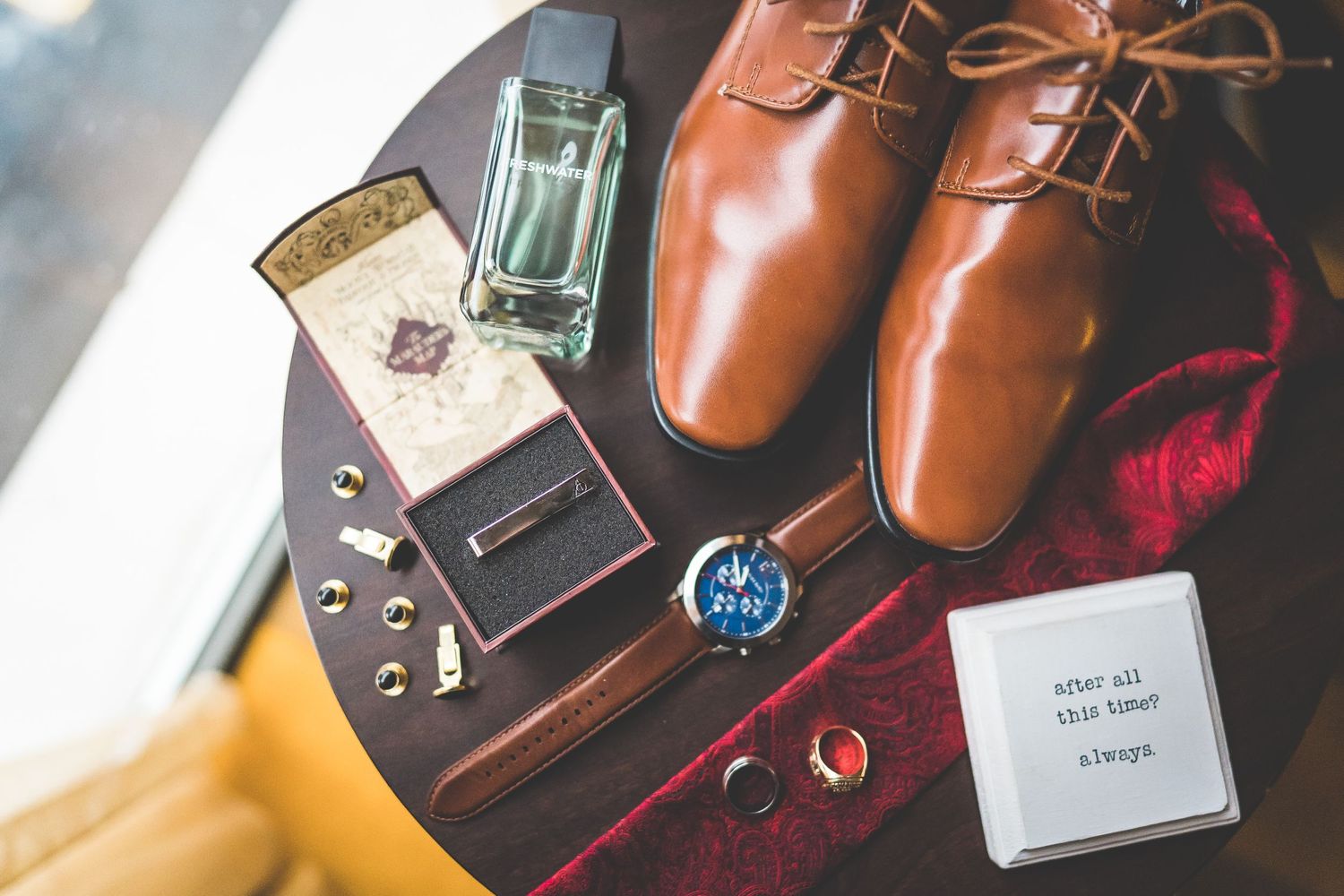 Groom's accessories including brown leather shoes, watch, and personal items arranged on surface.