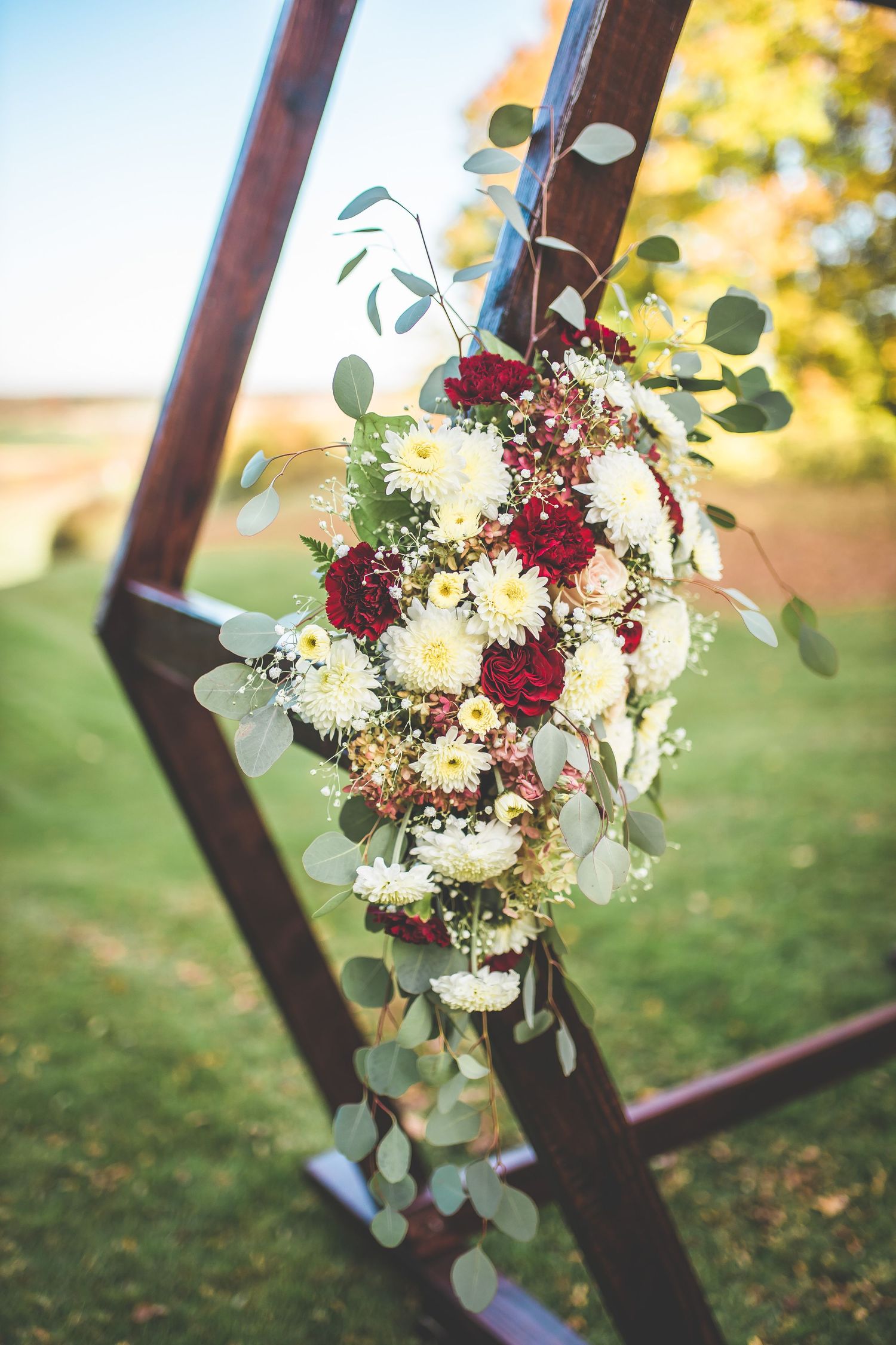Floral arrangement with burgundy roses and white daisies decorating a wooden arch.