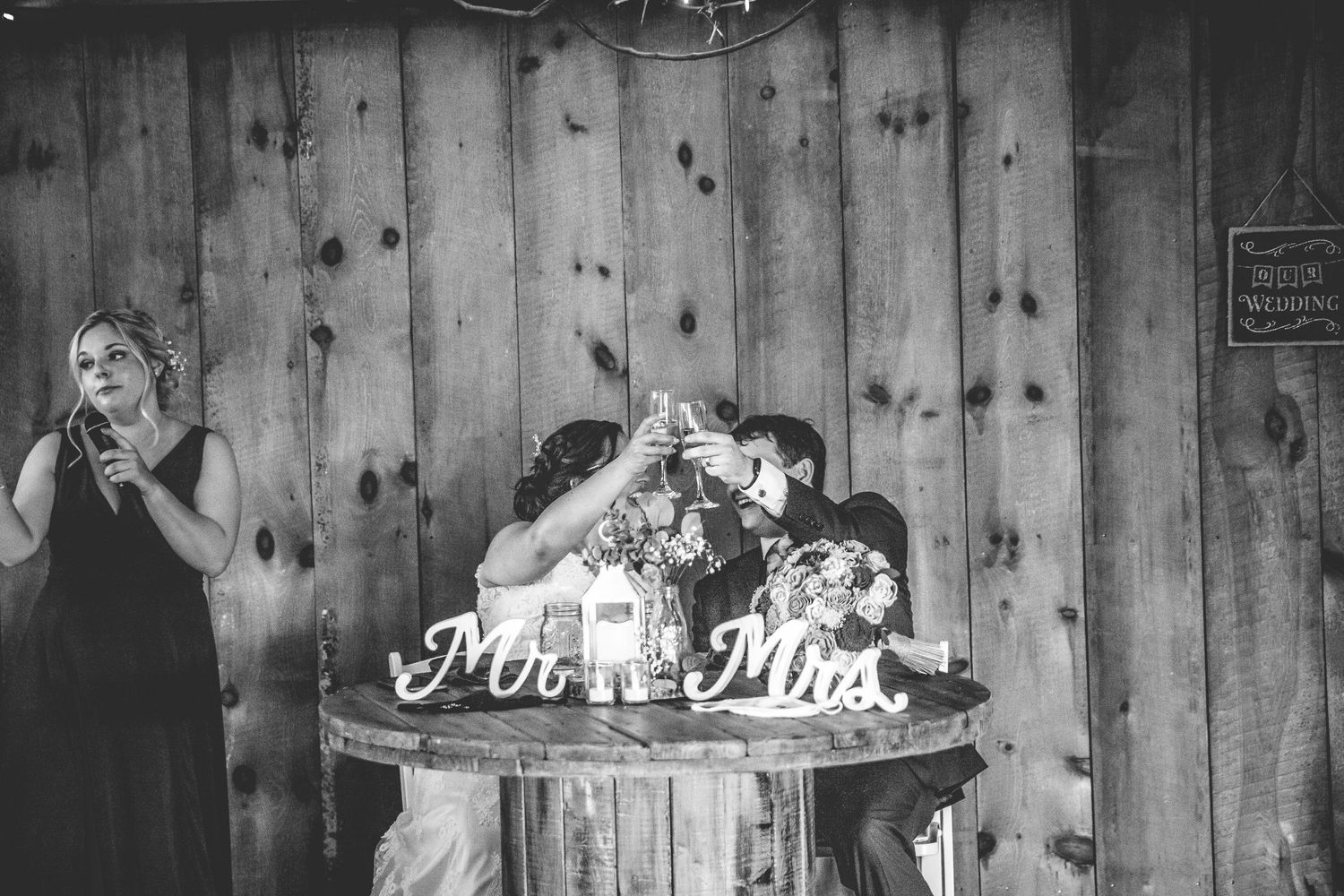 Wedding reception in rustic barn setting with wooden walls and decorative Mr & Mrs signage.