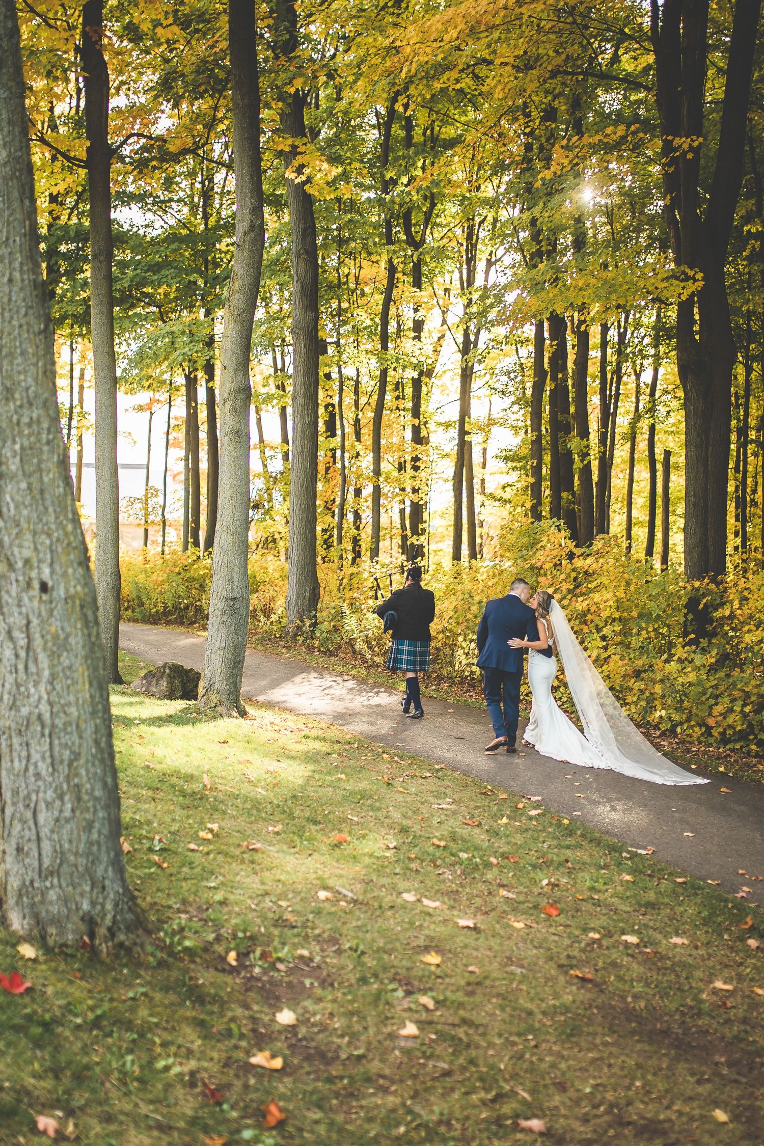 Wedding party walking through autumn forest with golden sunlight filtering through trees.