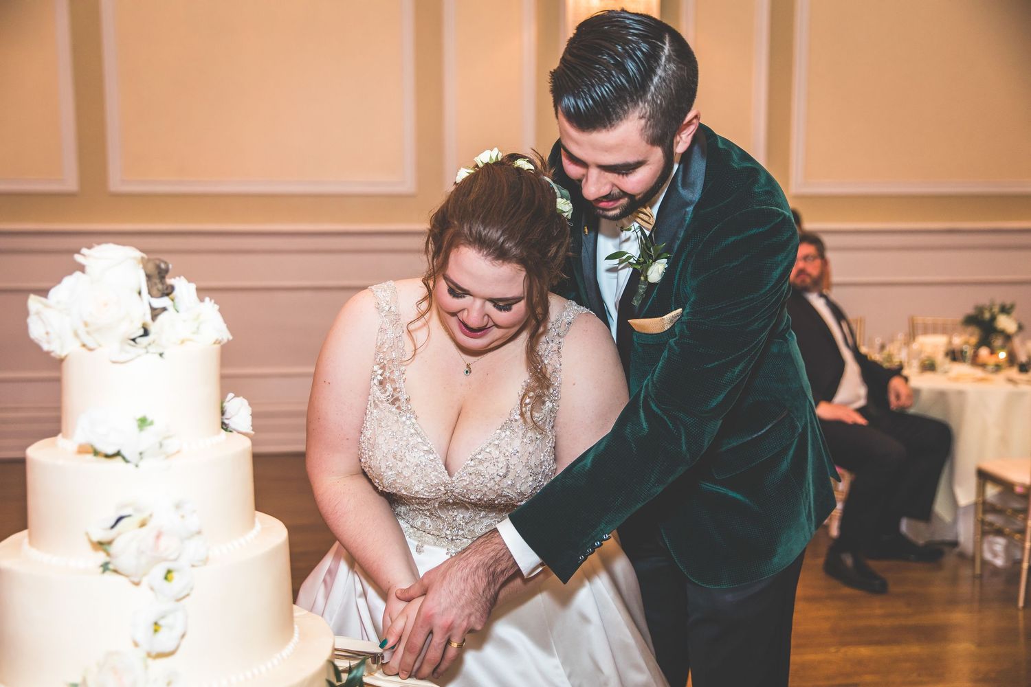 Wedding couple sharing a moment next to their elegant white tiered cake at the reception.