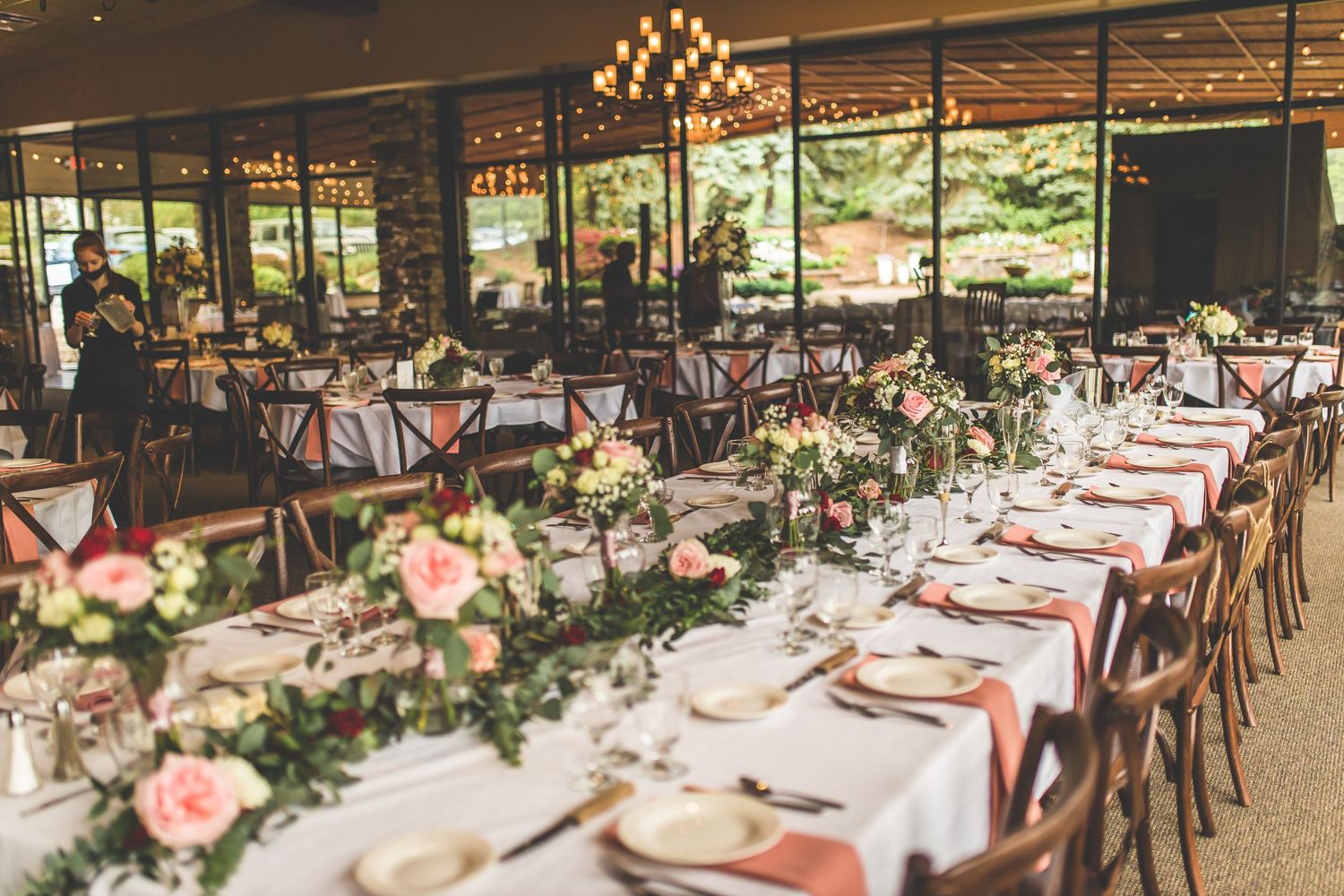 A beautifully decorated wedding reception venue with long tables, floral centerpieces and chandeliers.