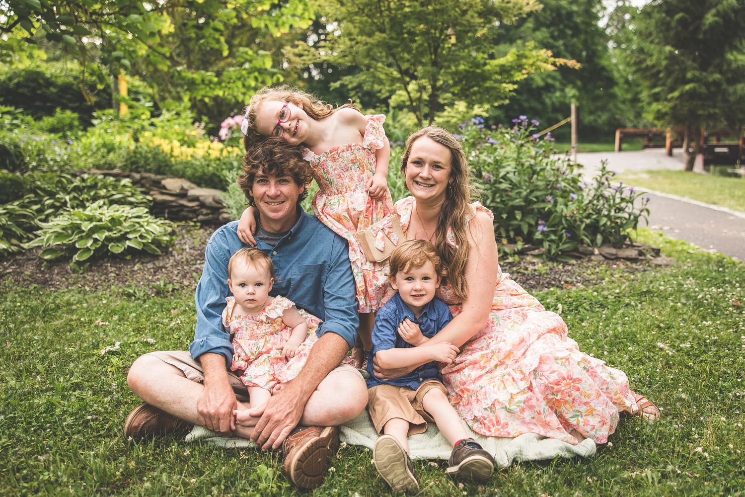 A happy family sits together on green grass in a park setting during a sunny day.