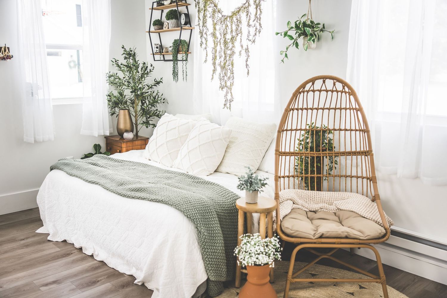 Bright boho-style bedroom with rattan chair, white bedding, and hanging plants.