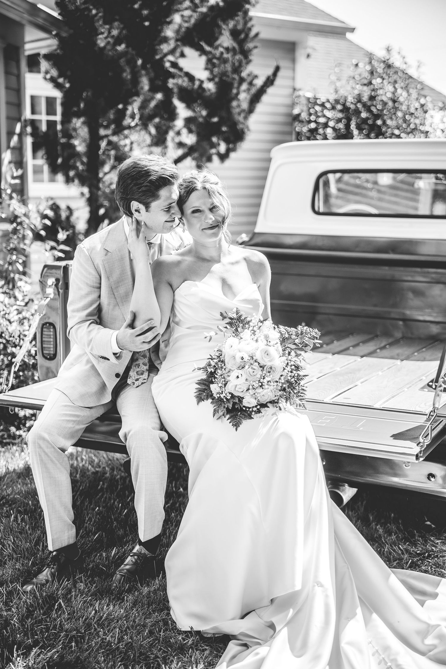 Black and white wedding portrait showing a couple sitting together on a classic car.