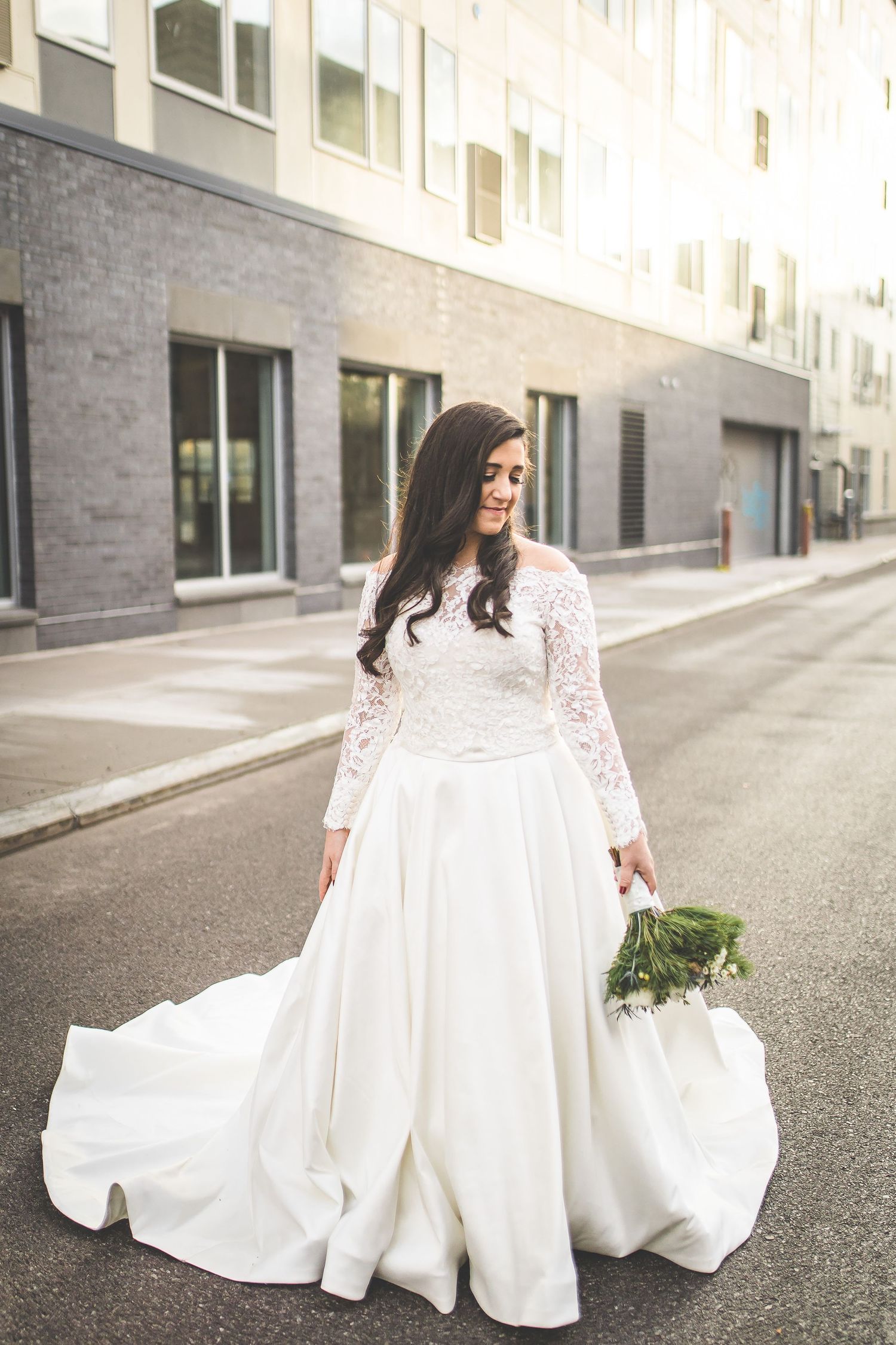 Elegant bride in lace sleeve wedding gown posing on urban street.