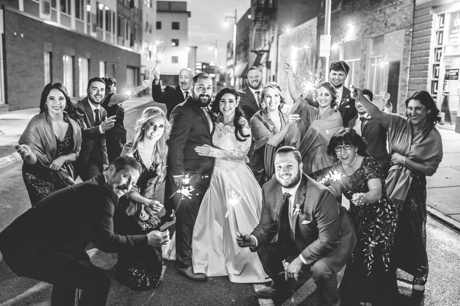 Black and white photo of wedding guests celebrating with sparklers at night.
