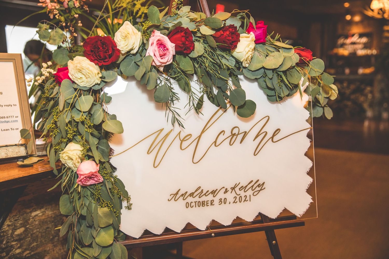 Elegant floral arrangements with red and pink roses decorating white wedding signage.