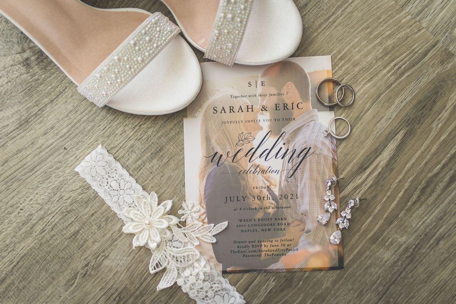 Wedding details including white shoes, lace garter, and an elegant invitation on a wooden surface.