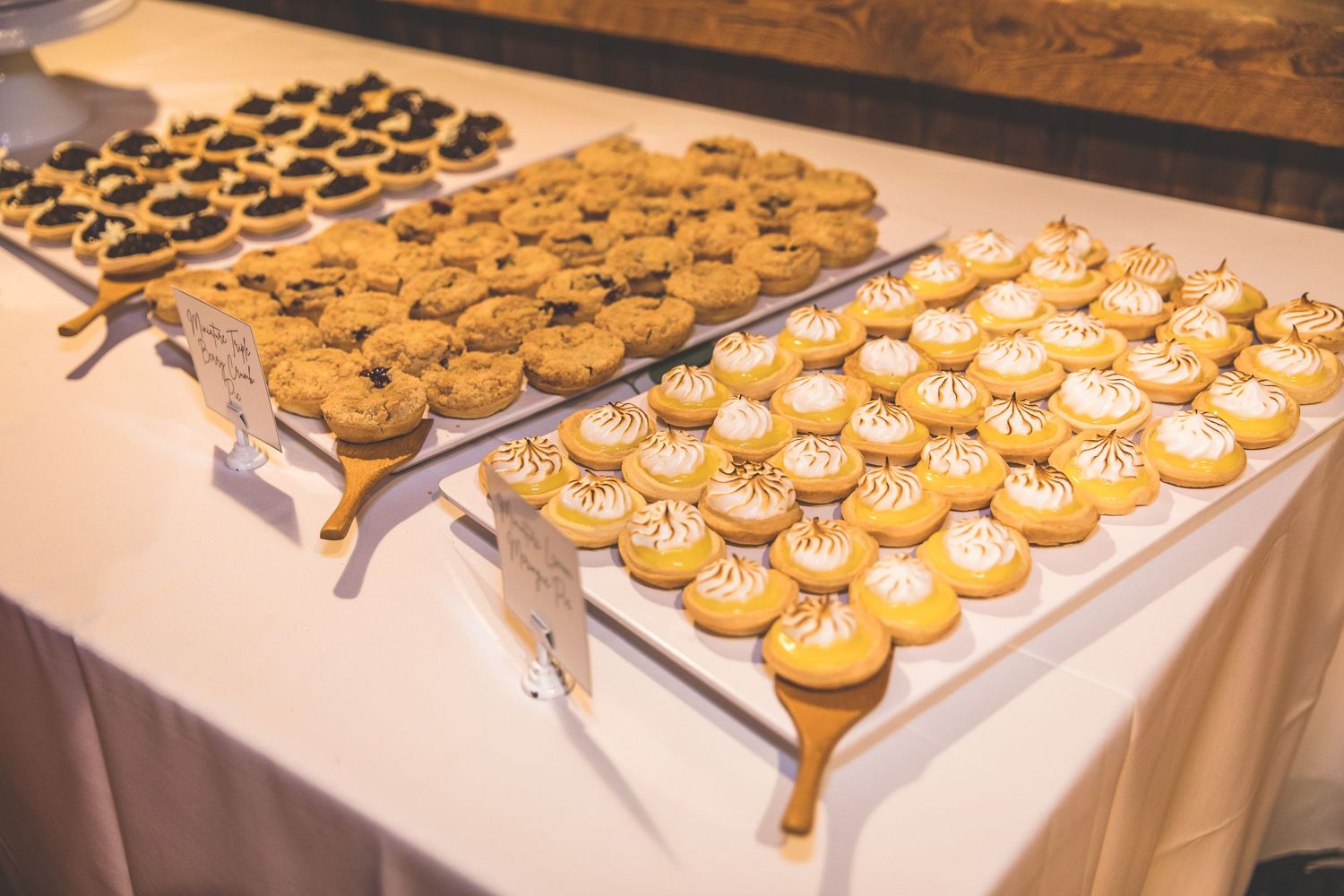 Multiple trays of mini desserts and cupcakes displayed on a wedding reception dessert table.