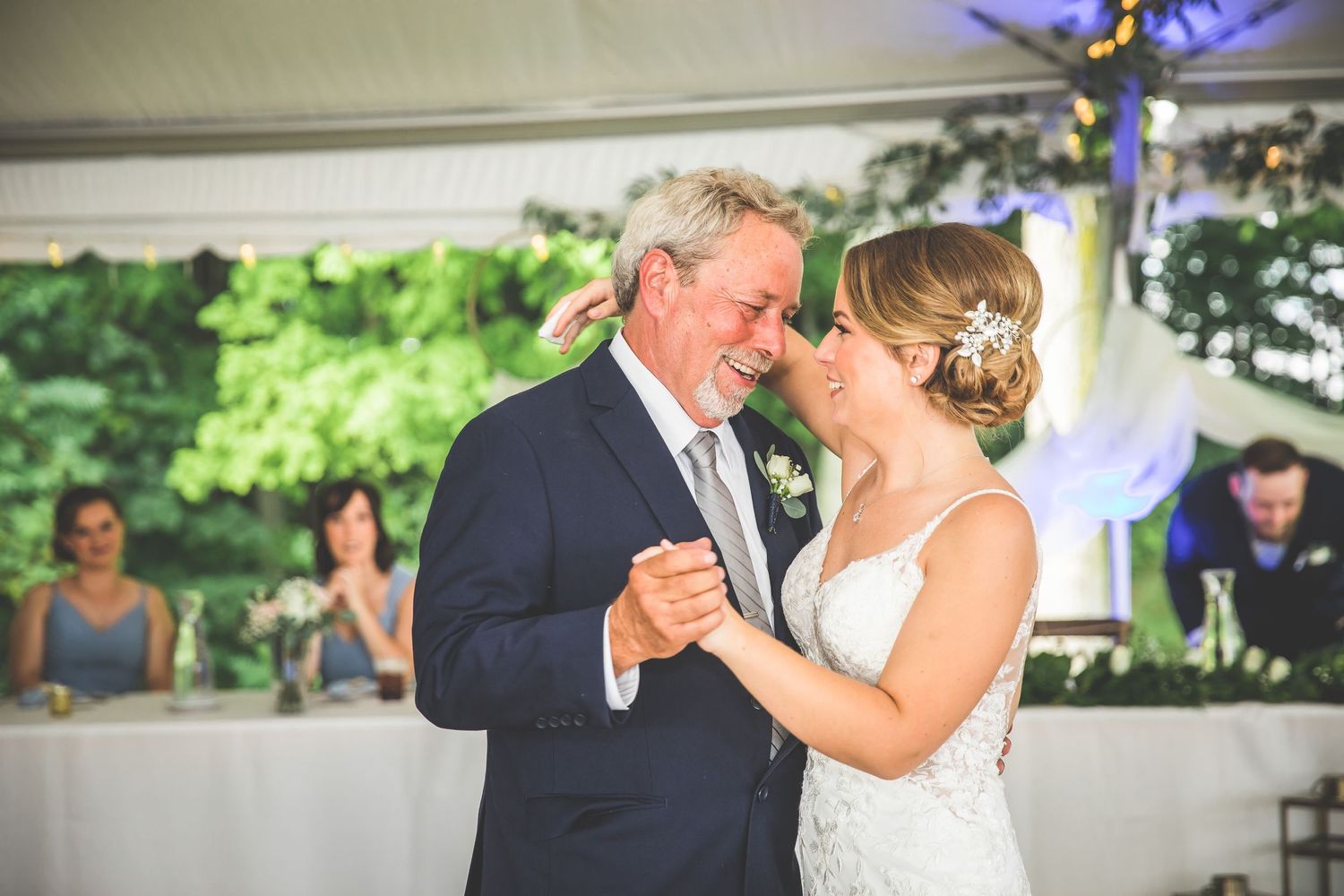 Couple shares romantic dance moments under tent with string lights and natural backdrop.