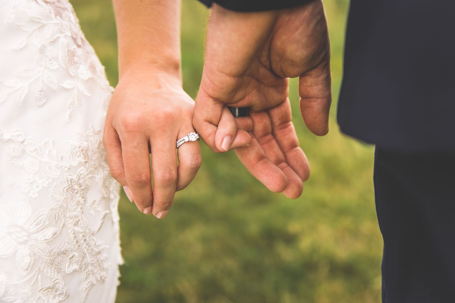 Close-up shot of couple holding hands showing wedding rings against lace dress details.