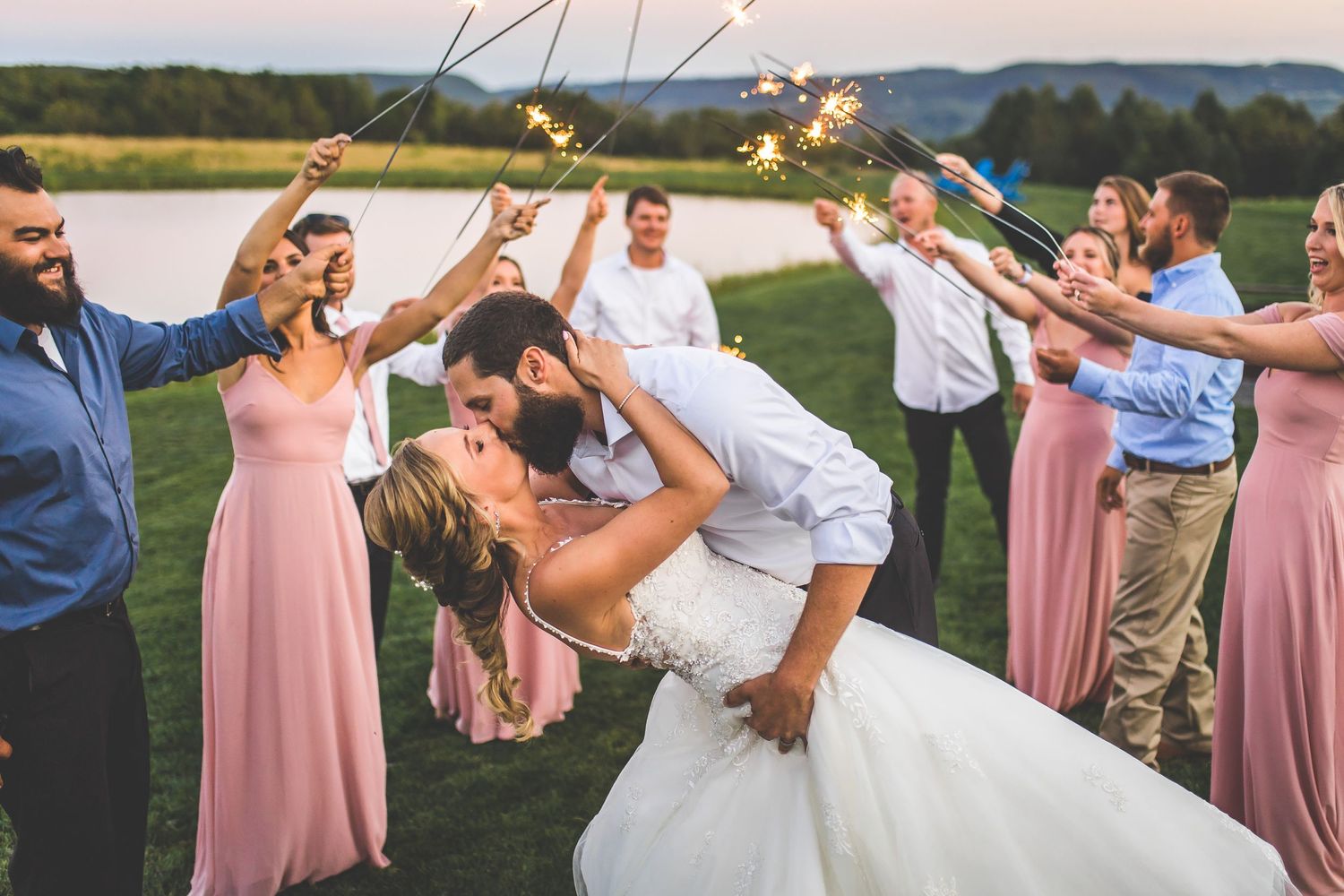 Wedding party creating a sparkler exit tunnel outdoors at dusk.