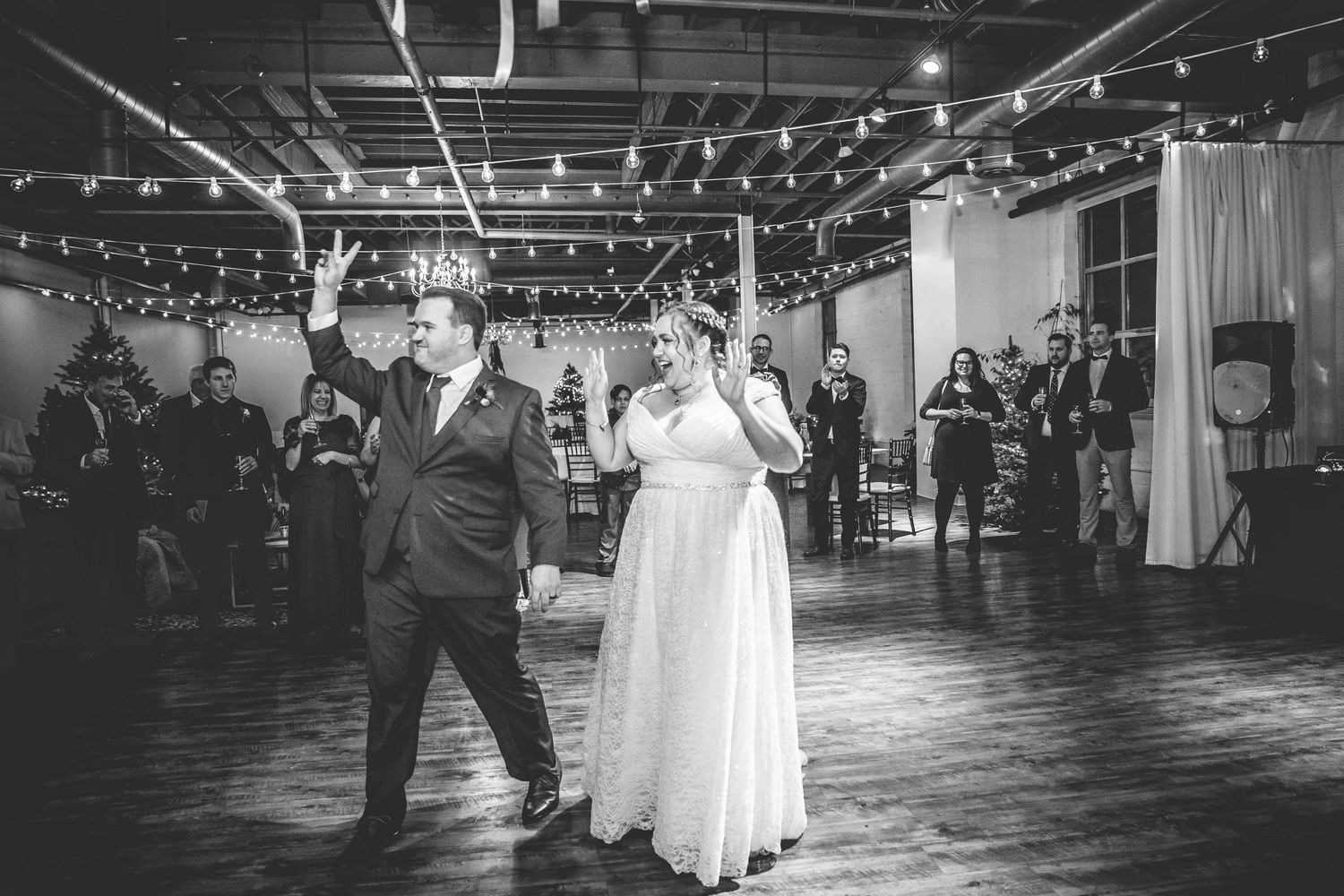 Wedding reception venue with string lights hanging from industrial ceiling creates romantic atmosphere.