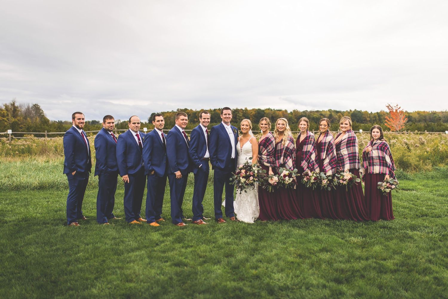 Wedding party lines up for formal photos in burgundy dresses and navy suits.