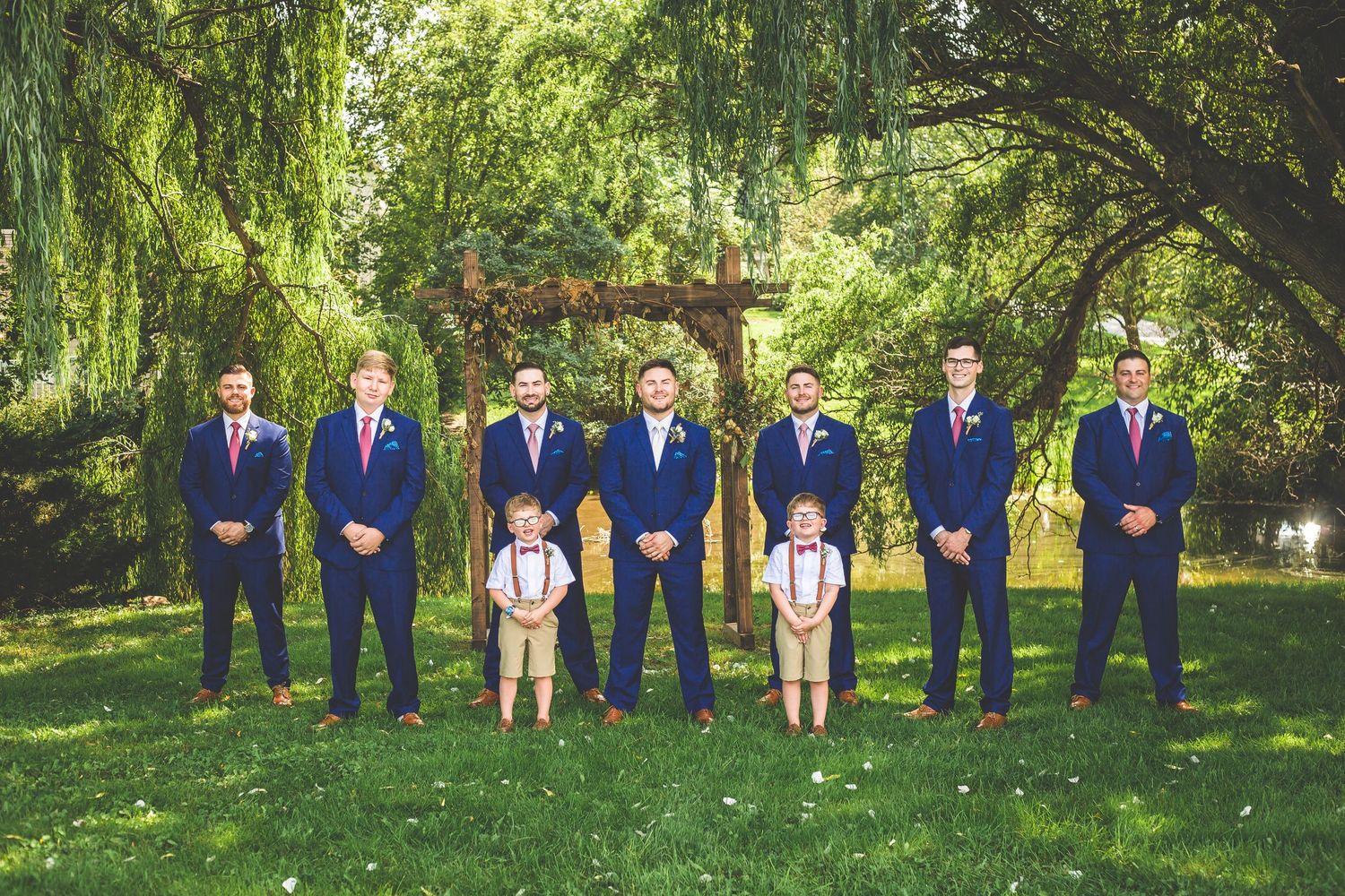 Wedding party in coordinated navy suits with two ring bearers posing in garden setting.