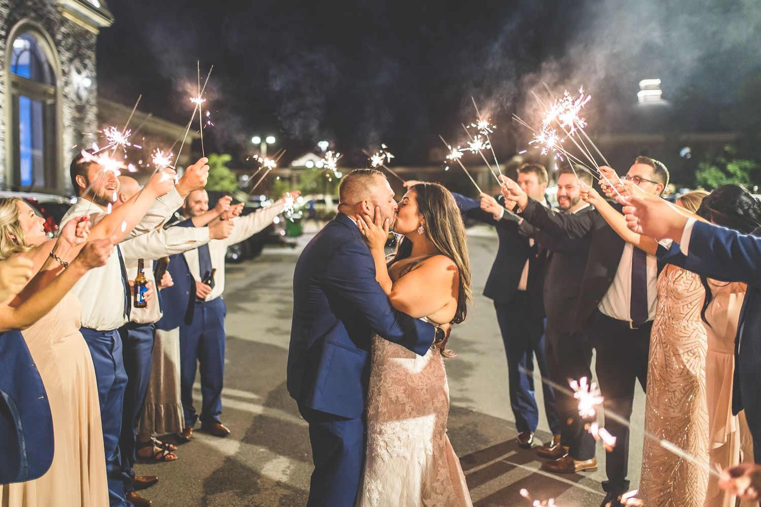 Wedding party and guests creating a sparkler tunnel during evening celebration.