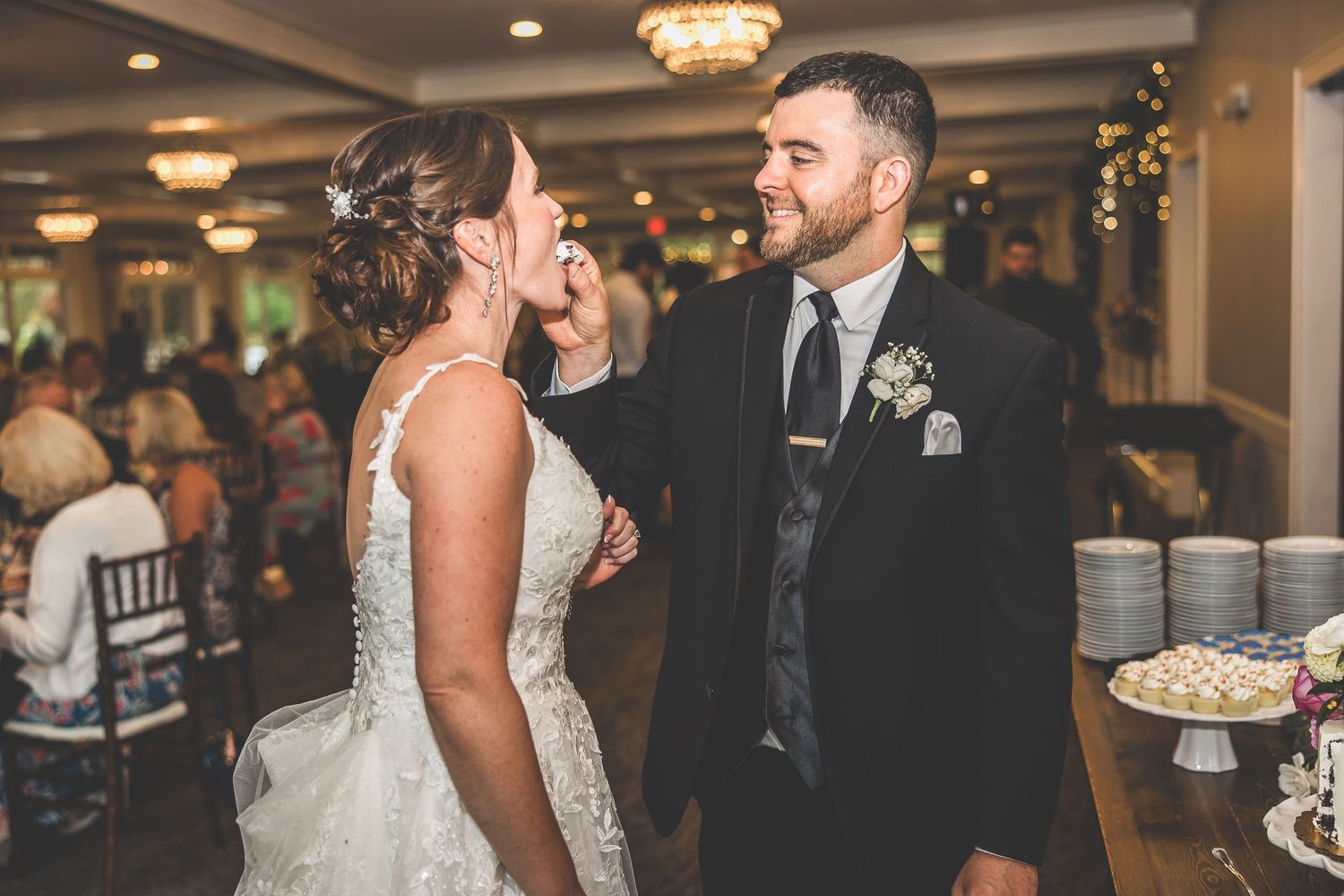 Couple feeds each other wedding cake during reception celebration.