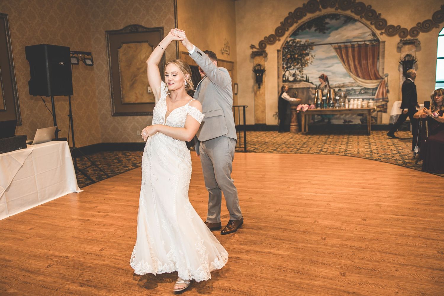 A couple shares their first dance at a wedding reception in an elegantly decorated ballroom with wooden floors.