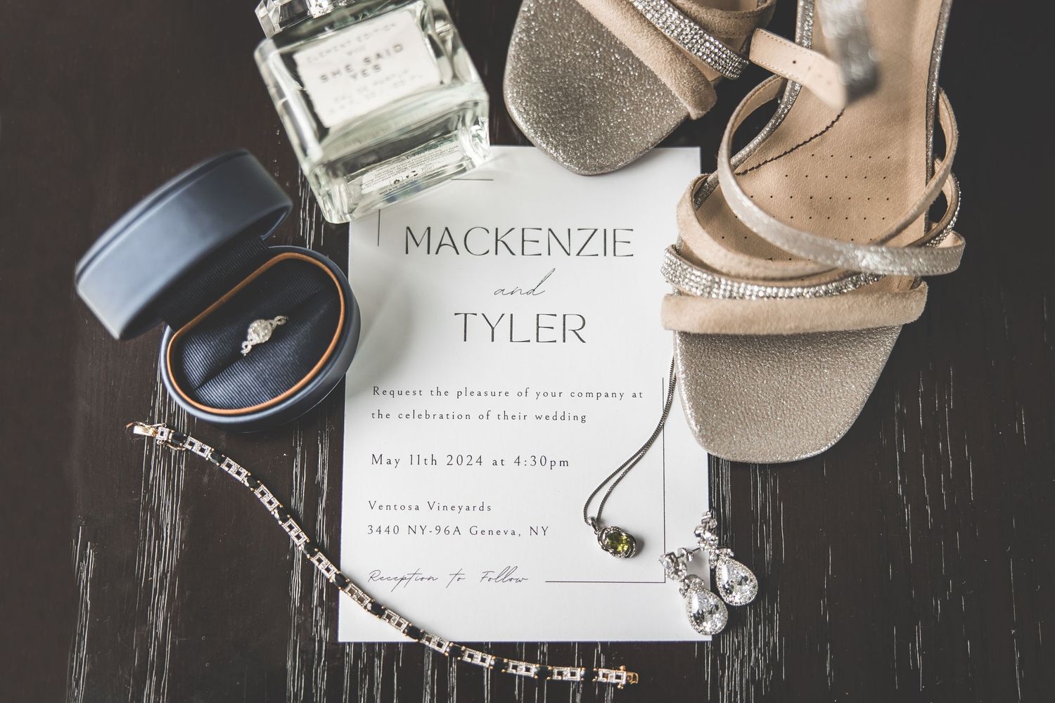 Wedding detail shot of name cards, rings, and accessories arranged on dark surface.