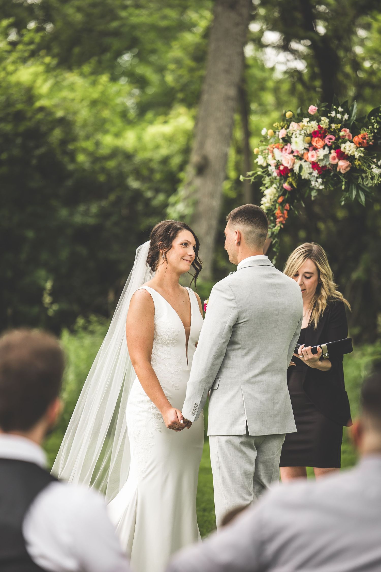 Wedding ceremony under floral arch with officiant and couple holding hands.