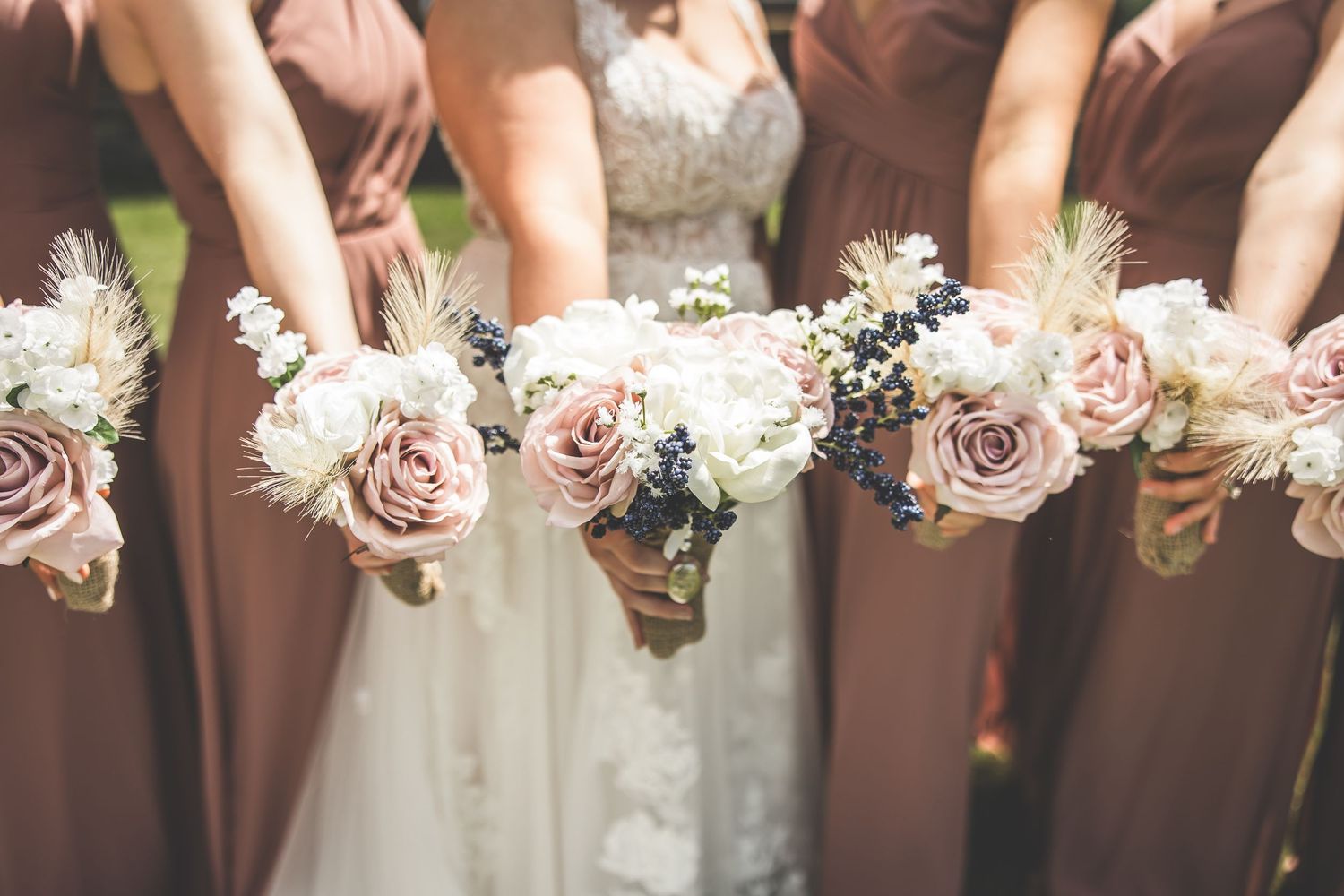 Close-up of pink and white wedding bouquets held against mauve bridesmaid dresses.